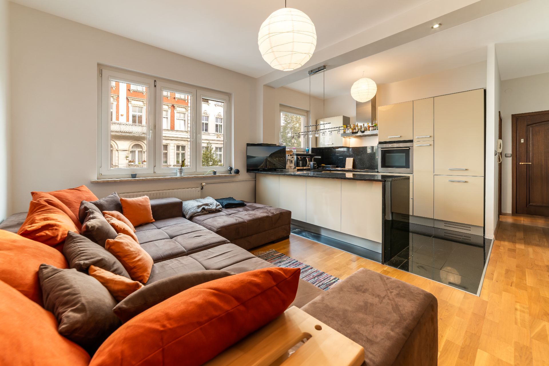 Modernes Wohnzimmer mit großer Eckcouch, offener Küche und viel Tageslicht durch große Fenster.
