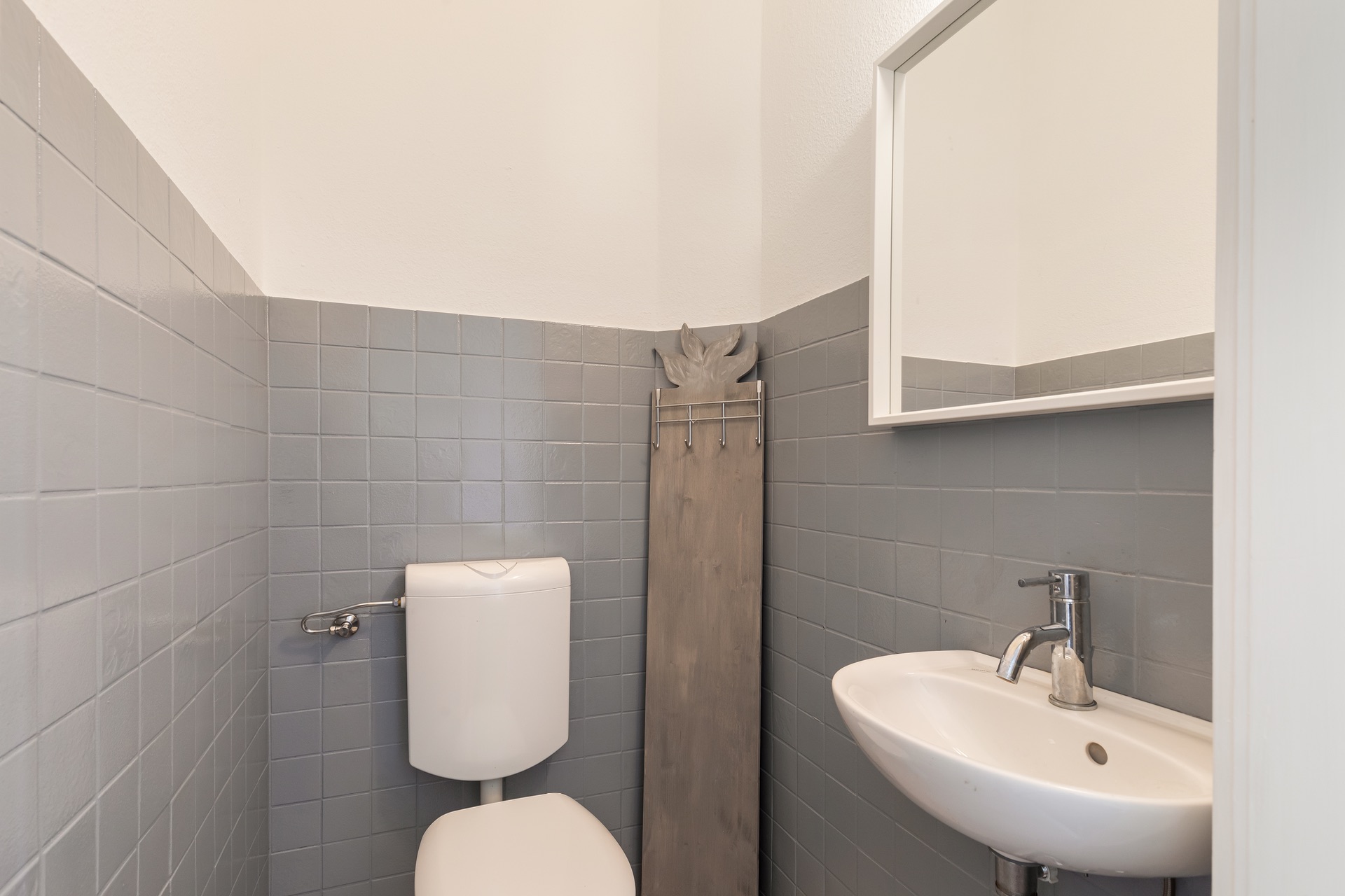 Kleines Bad mit Toilette, Waschbecken und grauen Fliesen an der Wand.