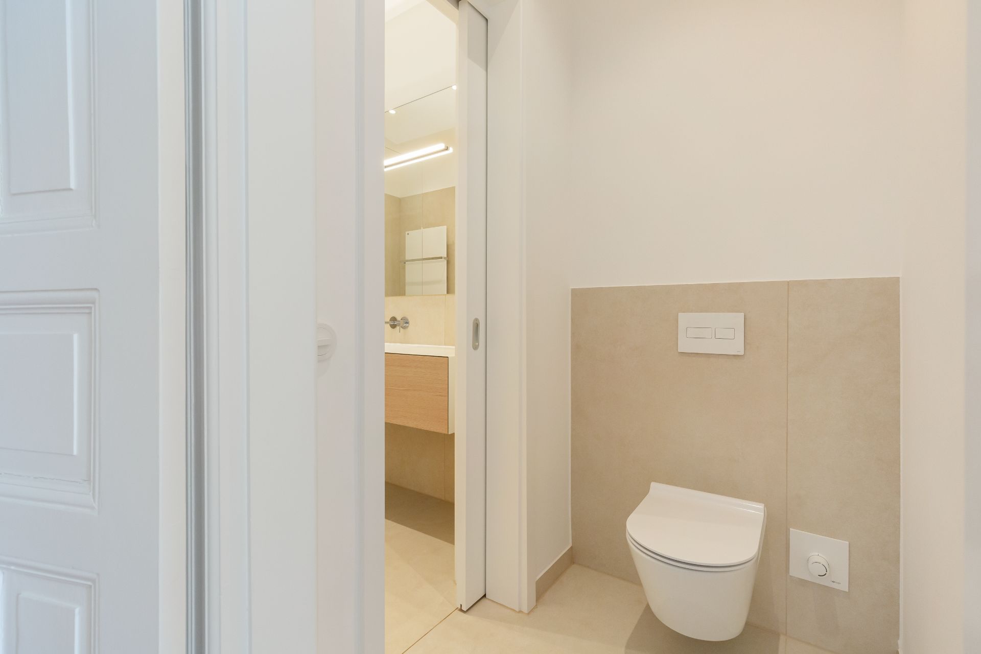 Modernes Badezimmer mit Wandtoilette und offenem Blick auf Waschbecken und Spiegel.