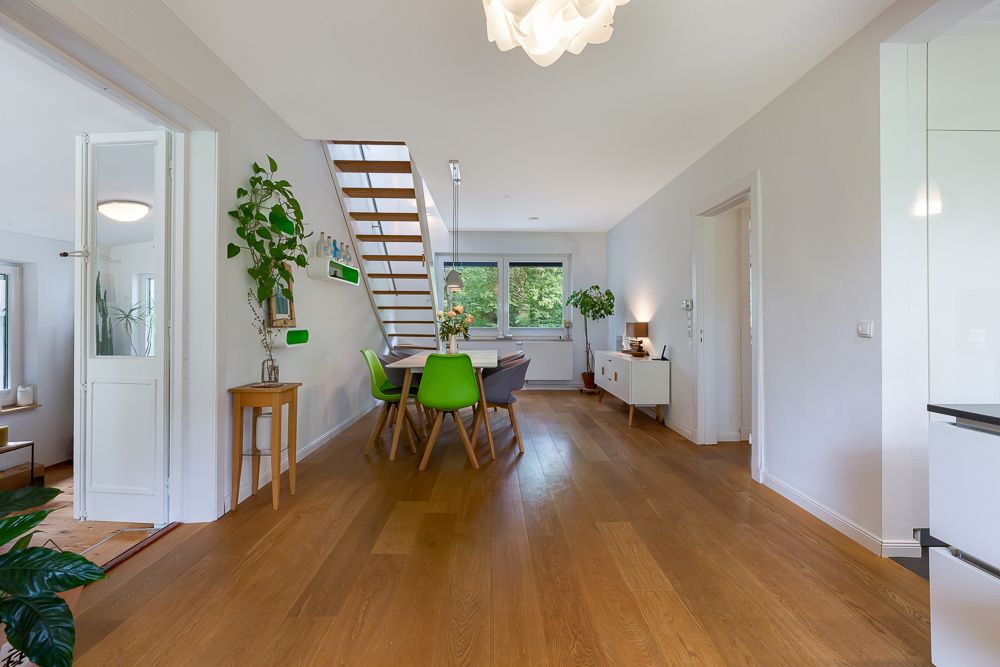 Heller Essbereich mit Holzboden, grünen Stühlen und Treppe, Blick auf Fenster im Hintergrund.