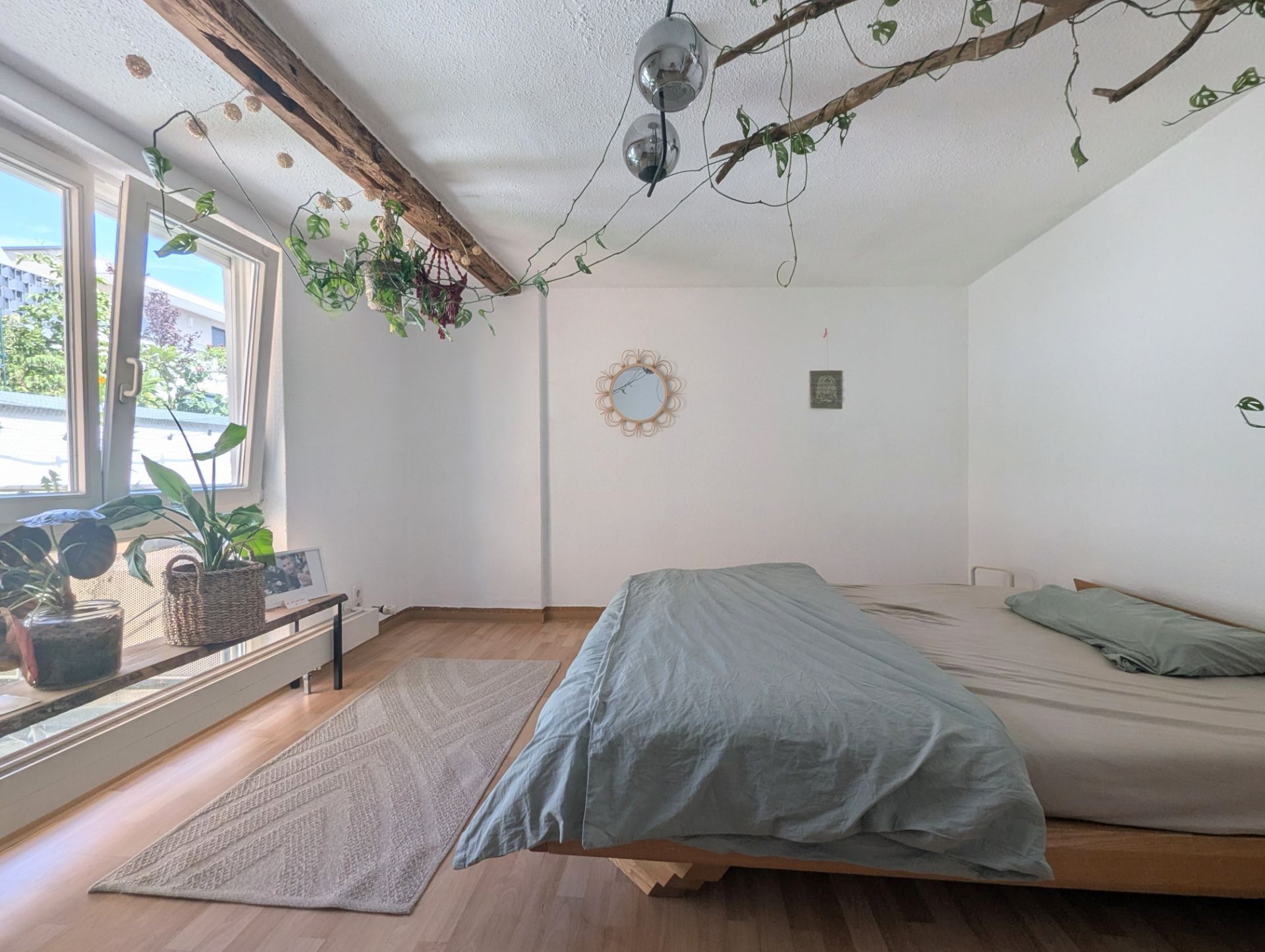 Helles Schlafzimmer mit großem Bett, Pflanzen und Holzbalken an der Decke.