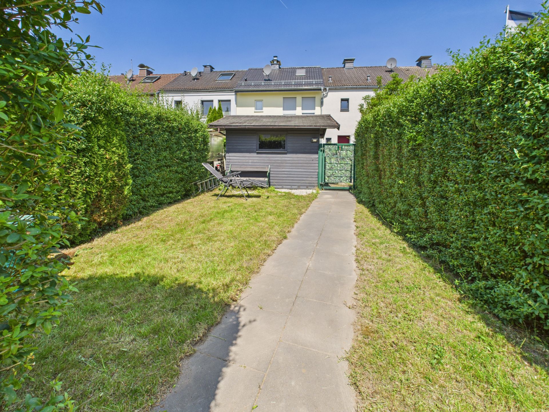 Gepflegter Garten mit Gartenhaus, Hecken und gepflastertem Weg.