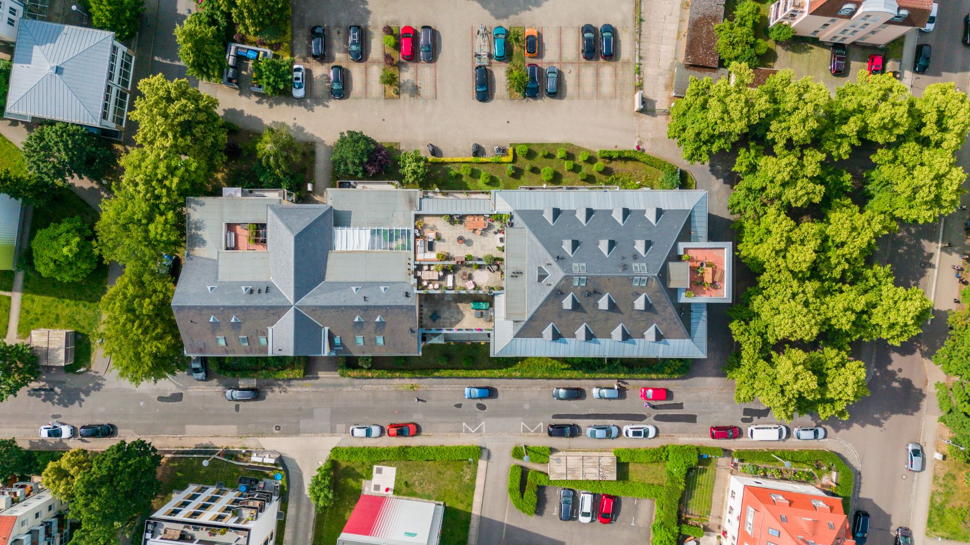 Luftaufnahme von Wohngebäuden mit parkenden Autos und umgebenden Bäumen.