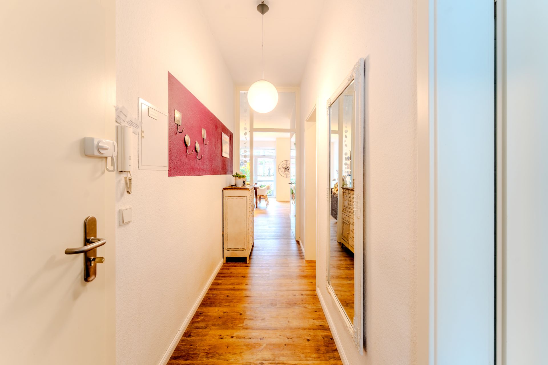 Heller Flur mit Holzfußboden, Spiegel, Kommode und runder Deckenlampe.
