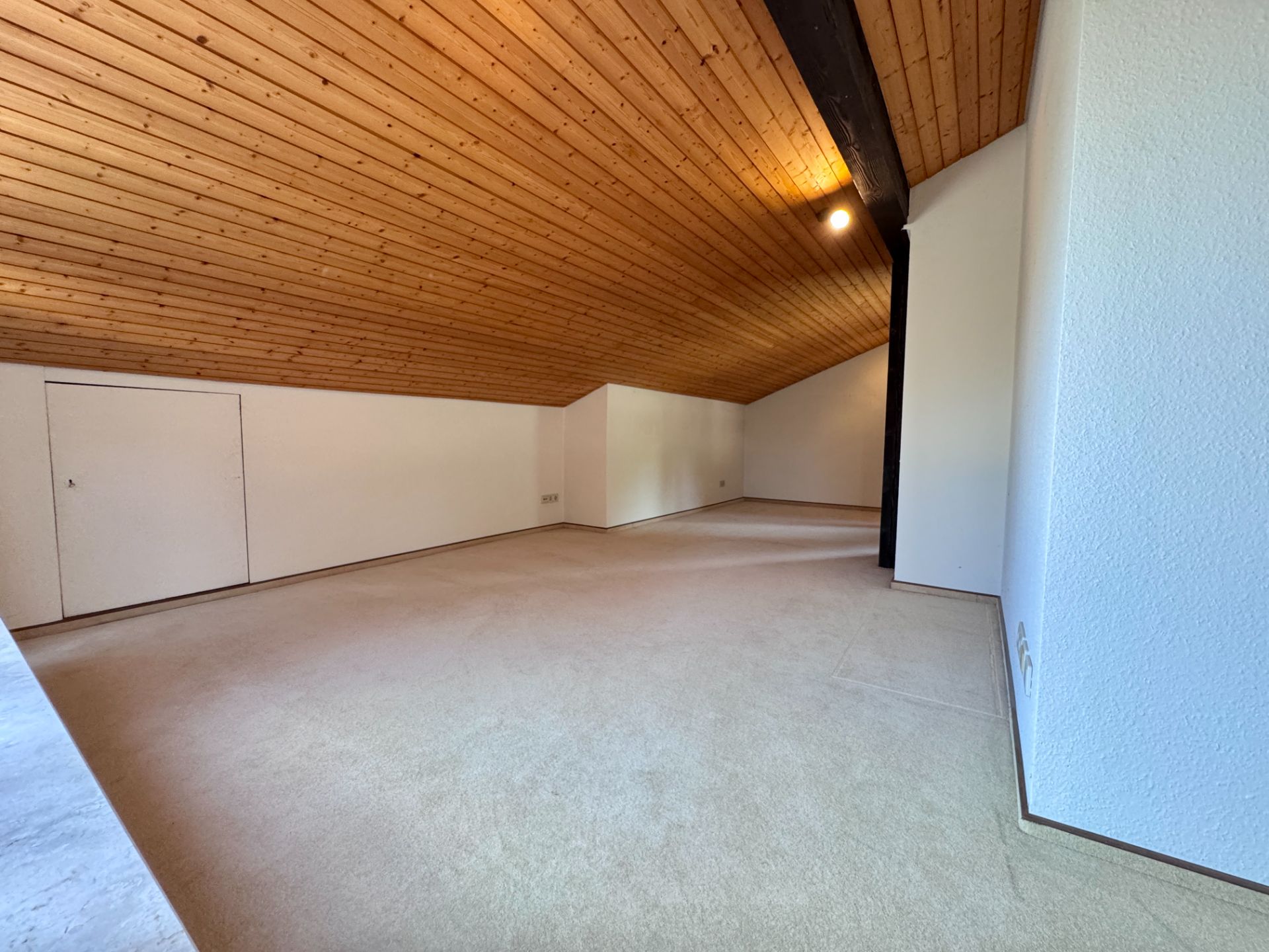Leerer Dachbodenraum mit schräger Holzdecke und weiß gestrichenen Wänden.