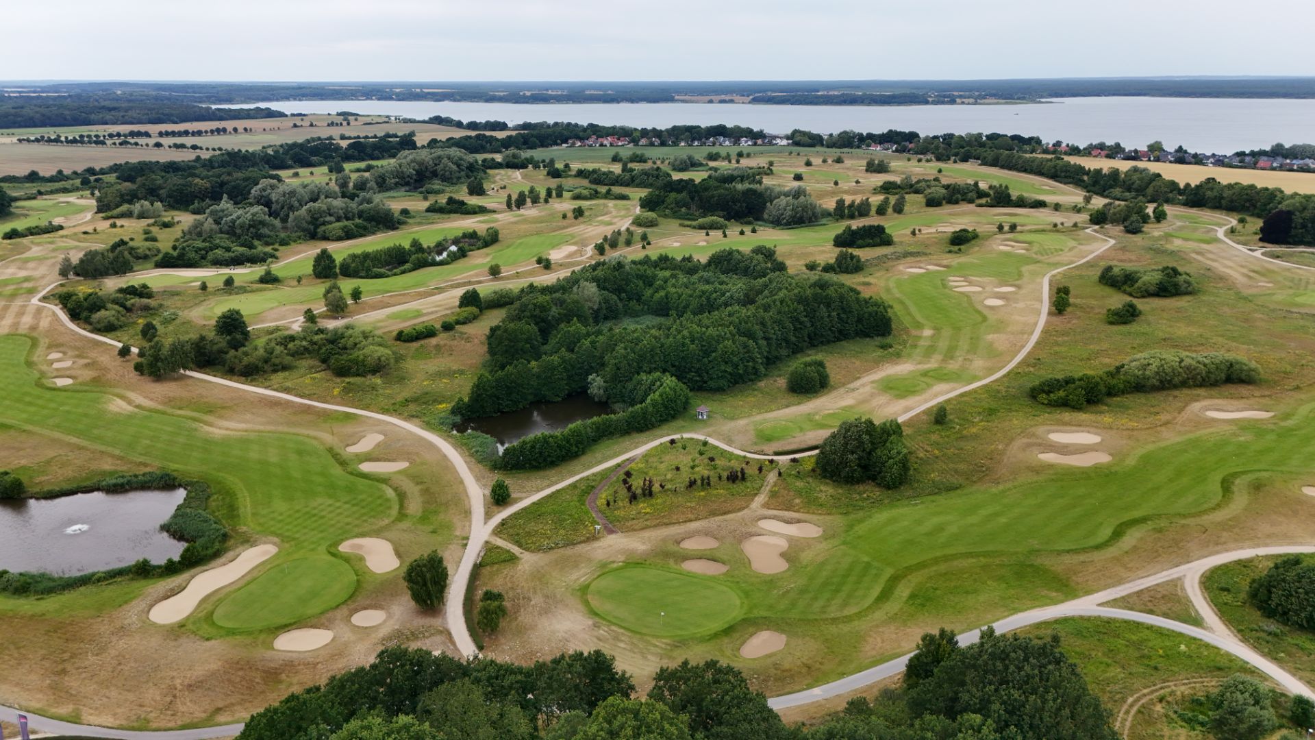 Luftaufnahme eines grünen Golfplatzes mit Wegen, Bäumen und Sandbunkern.