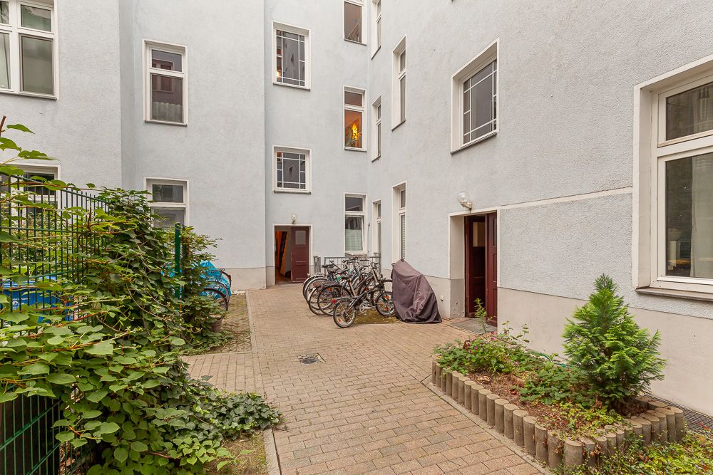 Gepflasterter Innenhof mit Fahrrädern, Pflanzen und mehreren Hauseingängen.