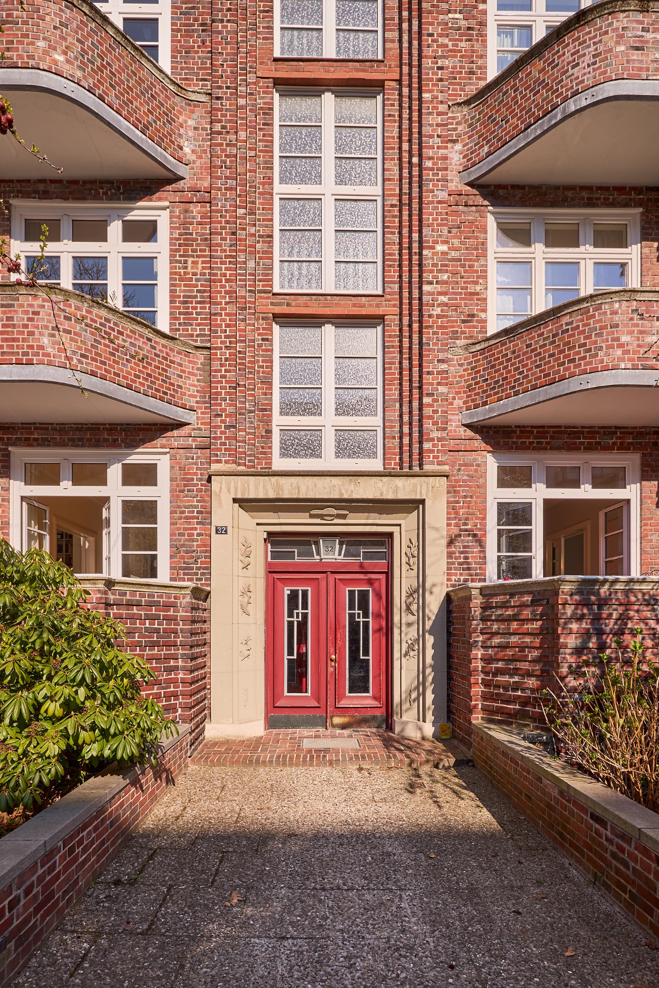 Eingang eines Wohnhauses mit roter Tür und Balkonen aus Backstein.