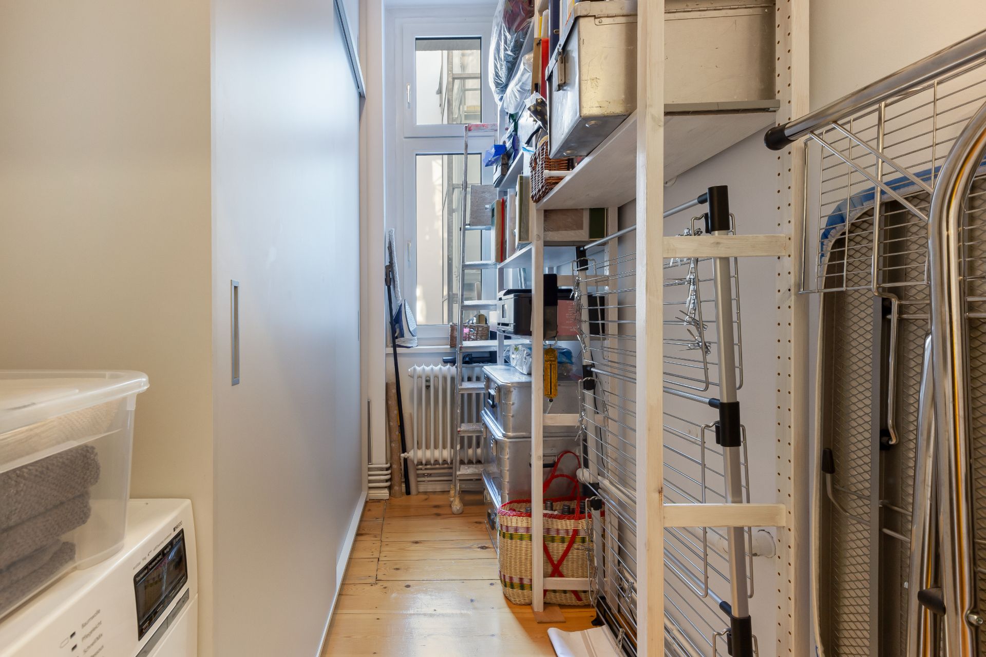 Schmaler Hauswirtschaftsraum mit Regalen, Wäscheständer und Fenster am Ende.