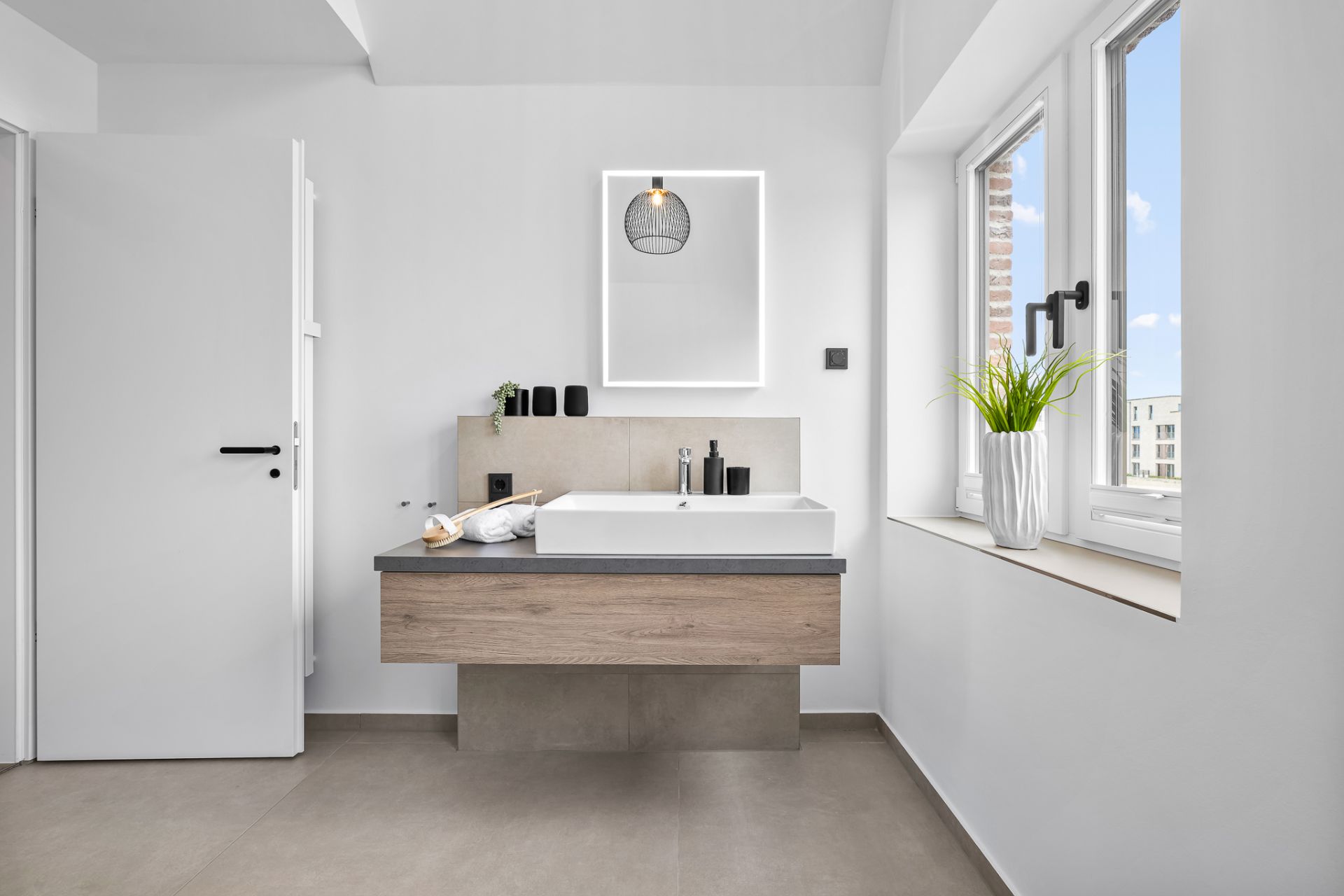 Modernes Badezimmer mit großem Waschbecken, beleuchtetem Spiegel und Fenster mit Blume im Topf.