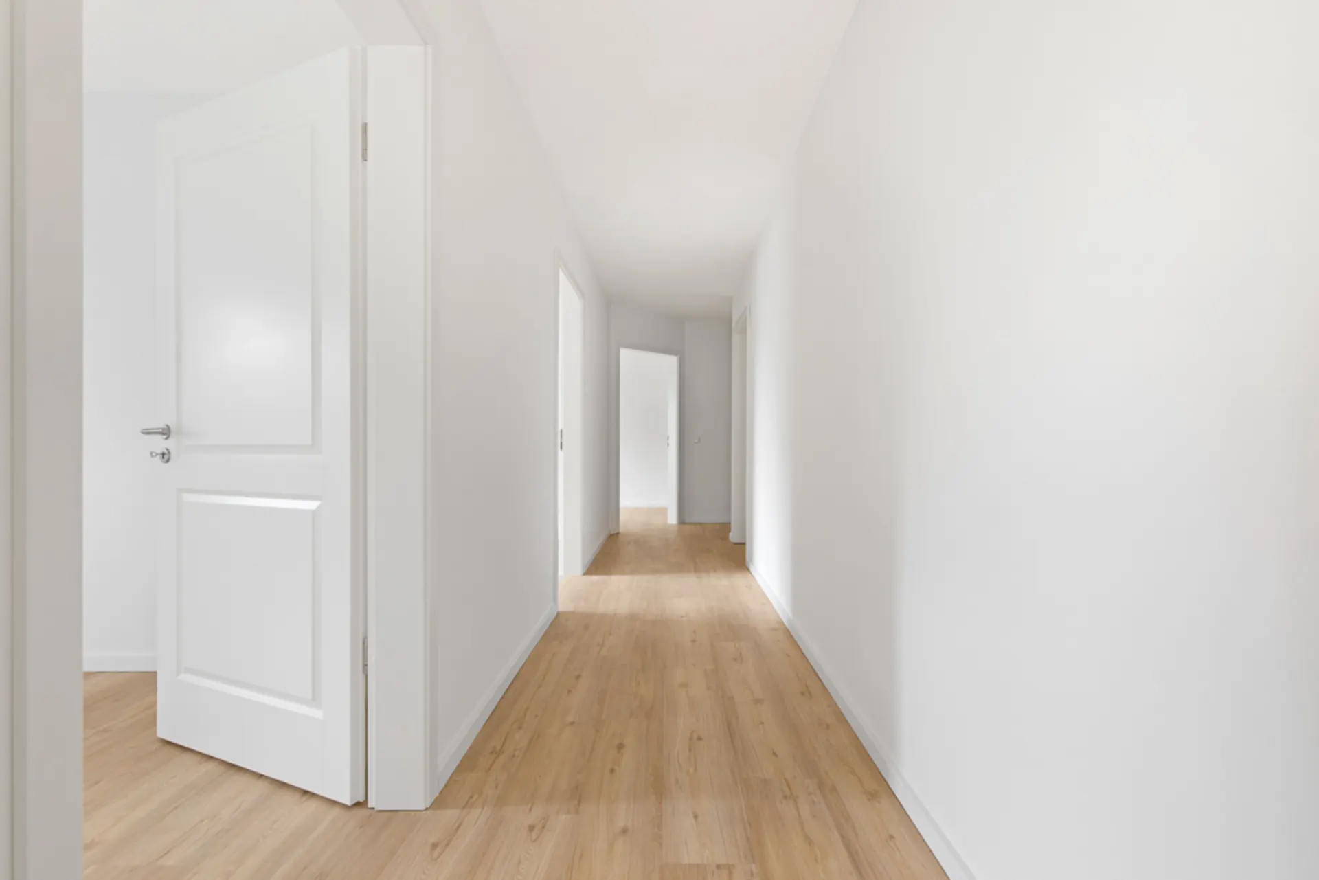 Langer, heller Flur mit Holzboden und weißen Wänden, mehrere offene Türen sichtbar.