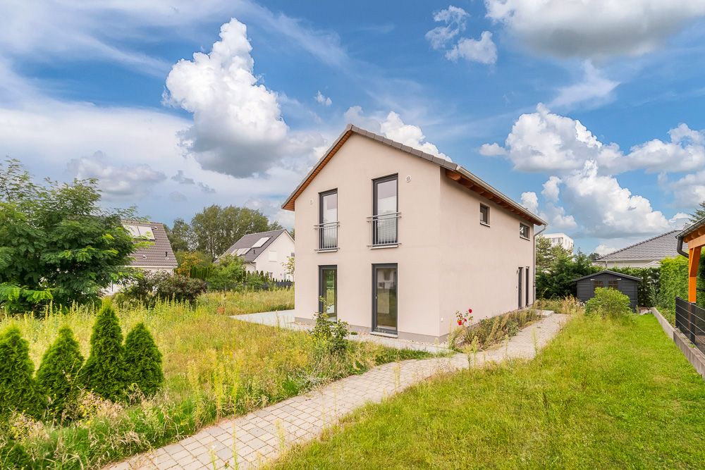 Modernes Einfamilienhaus mit Satteldach, großem Garten und gepflastertem Weg bei Tageslicht.