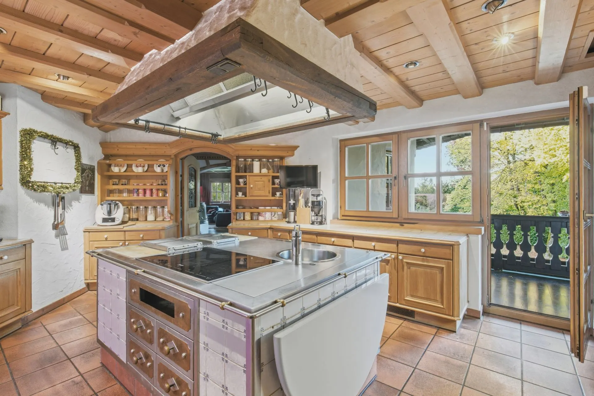 Helle Küche mit Holzmöbeln, Kochinsel, offenen Regalen und Zugang zu einem Balkon.
