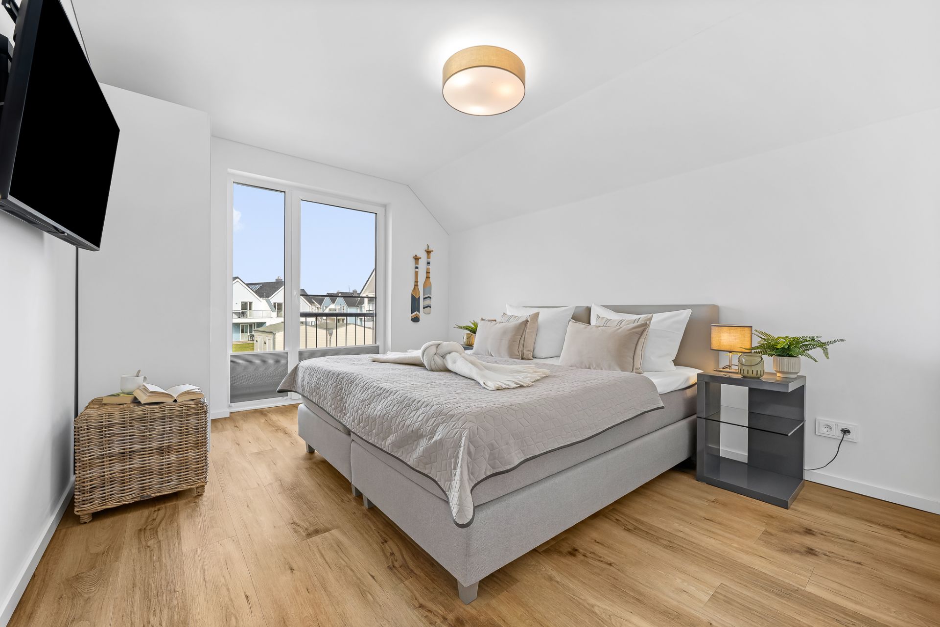 Helles Schlafzimmer mit Doppelbett, Fernseher, Holzboden und Zugang zu einem Balkon.