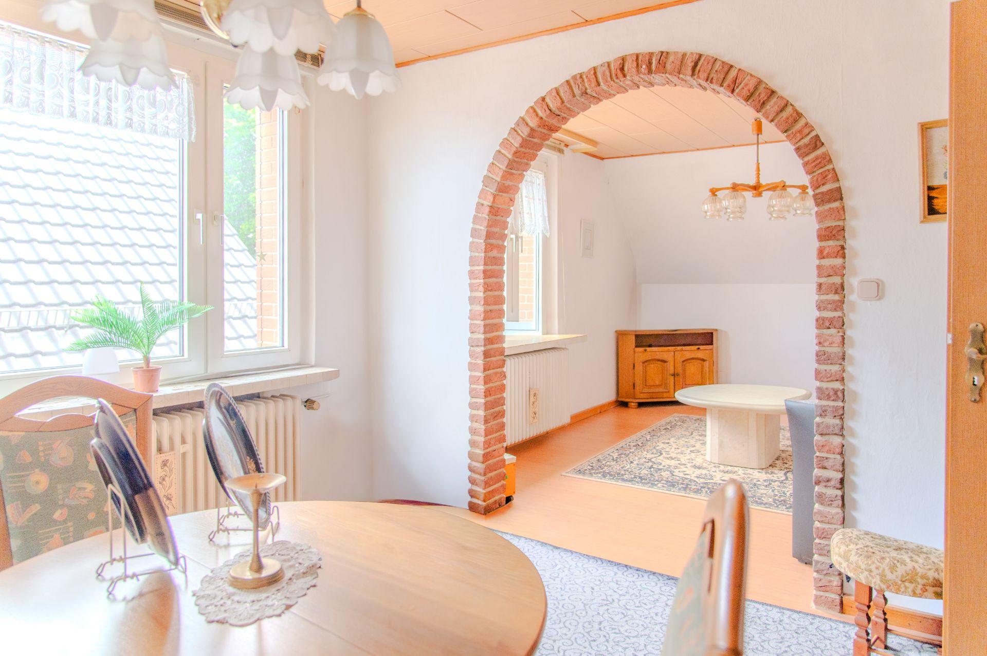 Helles Wohnzimmer mit gemauertem Rundbogen, Esstisch, Fenstern und Pflanzen.