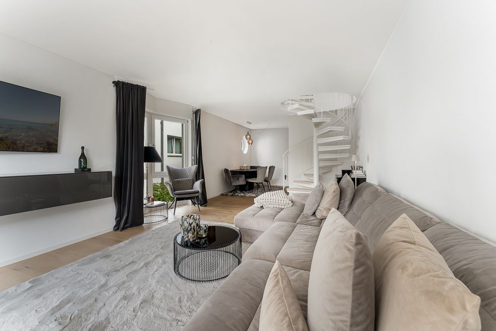Modernes Wohnzimmer mit grauem Sofa, Couchtisch und weißer Wendeltreppe.