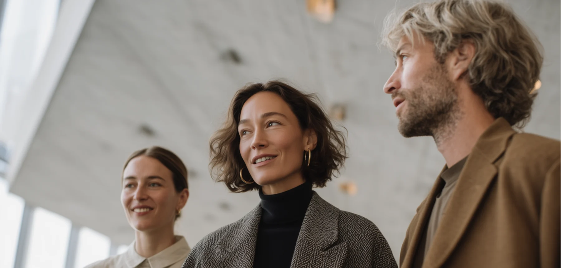 Drei Personen in Mänteln stehen zusammen in einem modernen Innenraum.