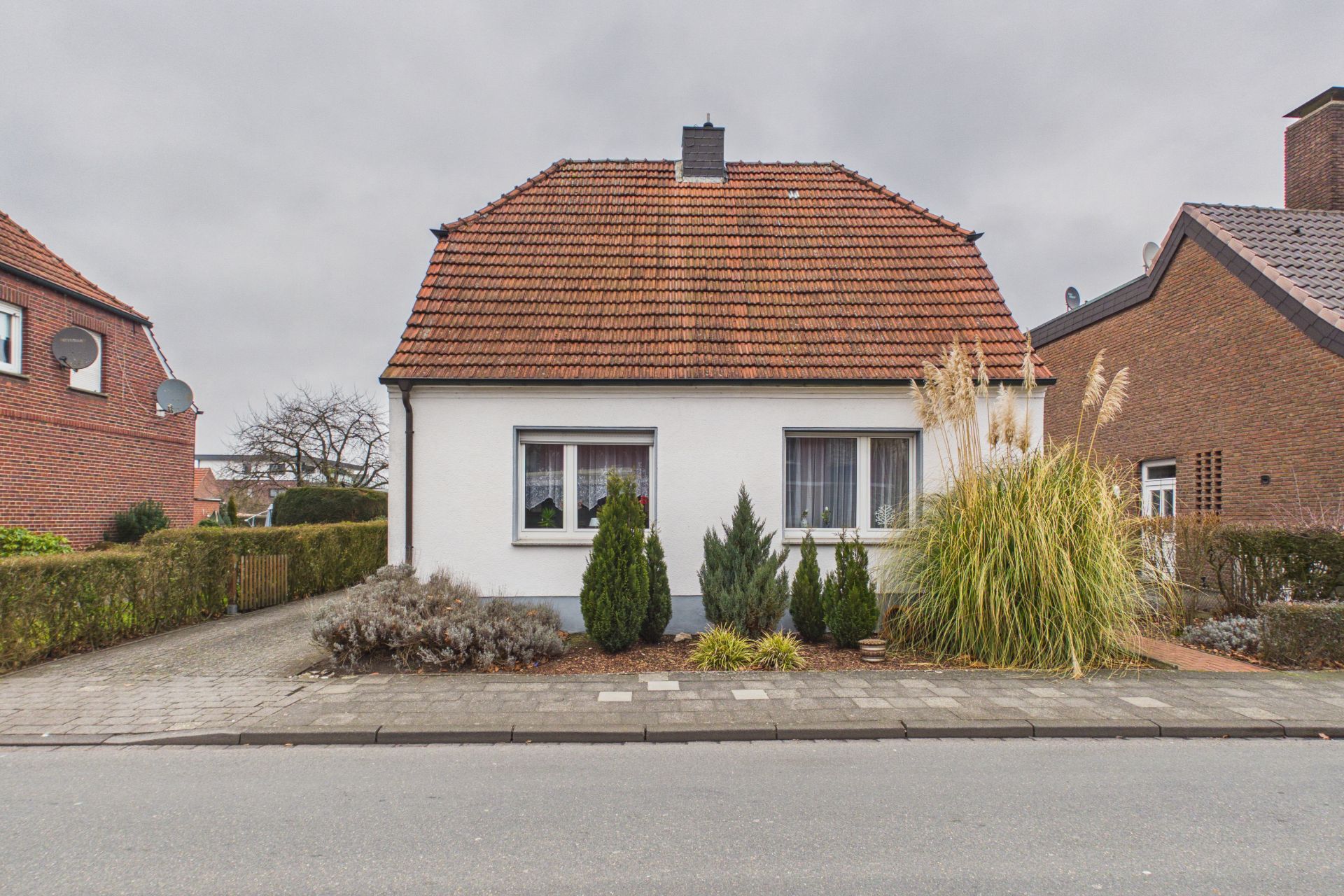 Einfamilienhaus mit rotem Dach und Vorgarten, frontal von der Straße aus gesehen.
