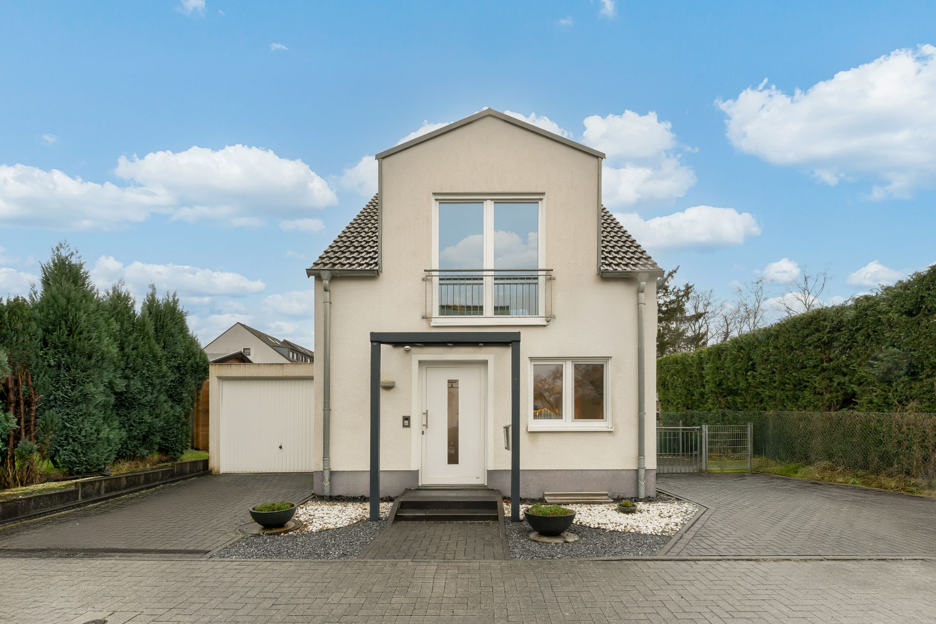 Modernes Einfamilienhaus mit großem Fenster über dem Eingang, Einfahrt und gepflegtem Vorgarten.