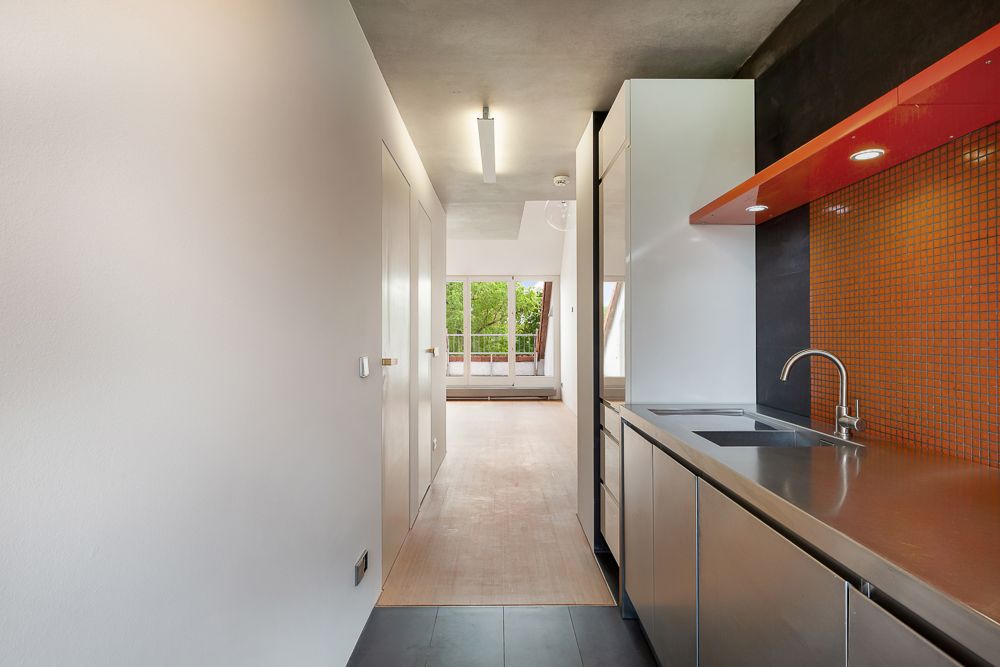 Moderne Küche mit Edelstahlspüle und orangefarbener Rückwand, Flur und Fenster im Hintergrund.