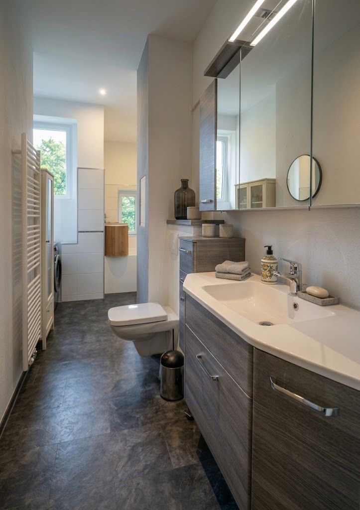 Modernes Badezimmer mit Waschtisch, Spiegel, Hängetoilette und großem Fenster.