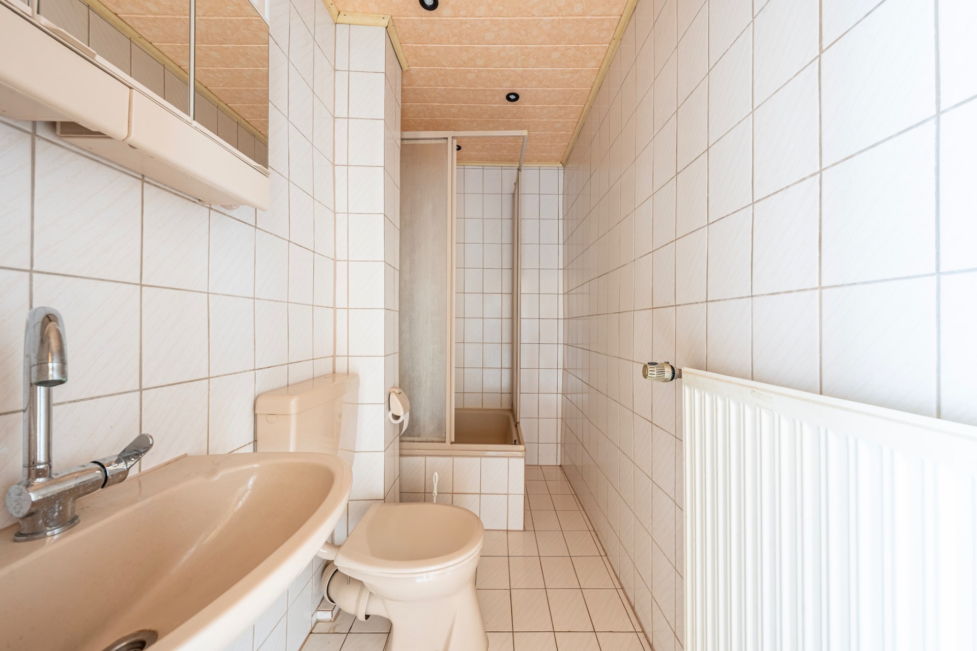 Schmales Badezimmer mit Waschbecken, Toilette, Dusche und weiß gefliesten Wänden.