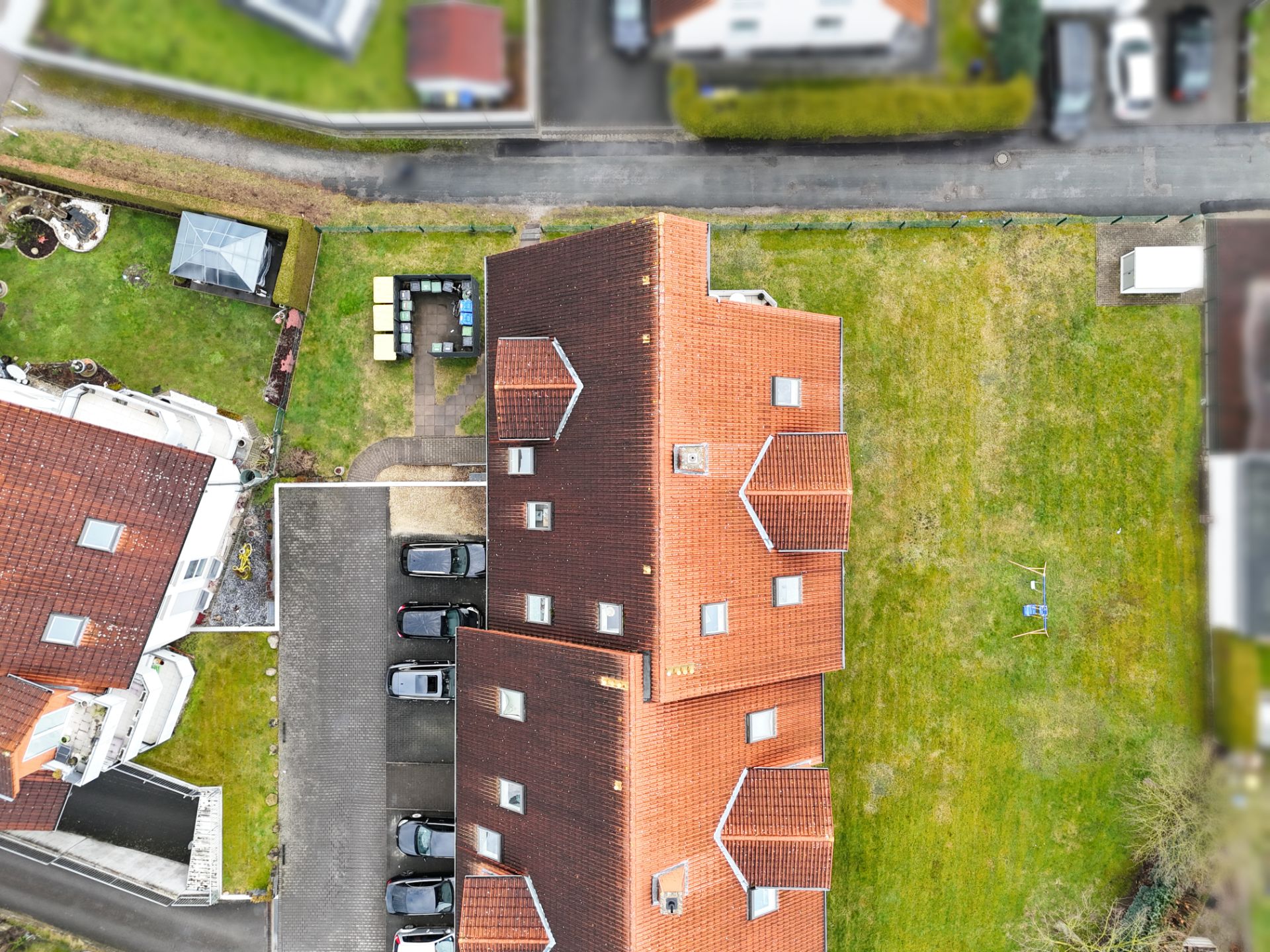 Luftaufnahme eines Wohnhauses mit rotem Dach, Garten und angrenzendem Parkplatz.
