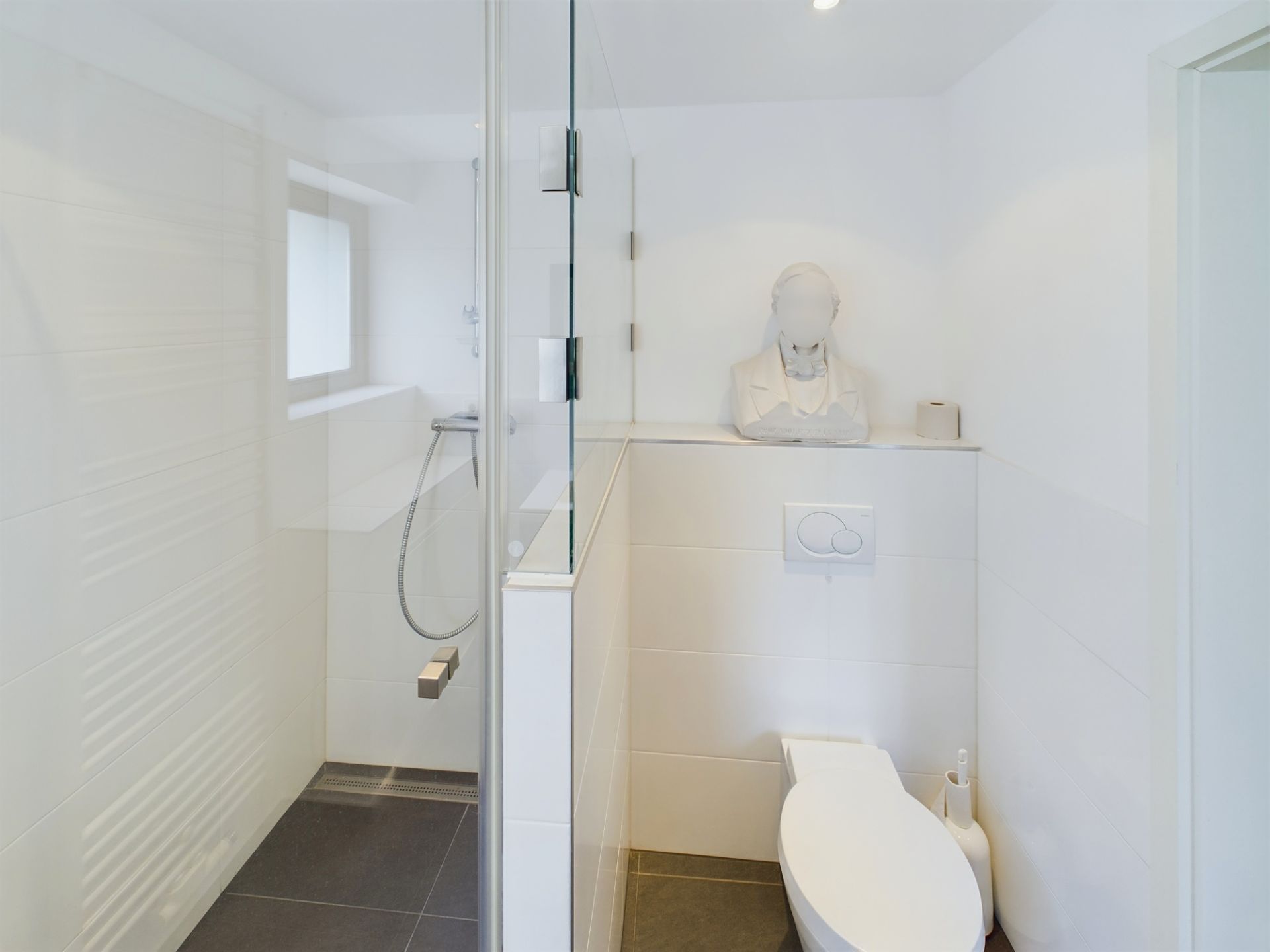 Modernes, weißes Badezimmer mit Toilette, Dusche und einer Büste auf einem Regal.