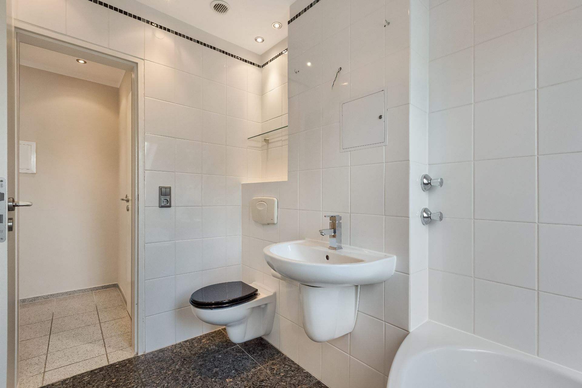 Modernes Badezimmer mit weiß gefliesten Wänden, Waschbecken, Toilette und Badewanne.