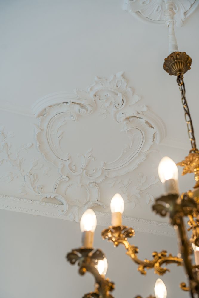 Stuckverzierte Decke mit einem Teil eines Kronleuchters im Vordergrund.
