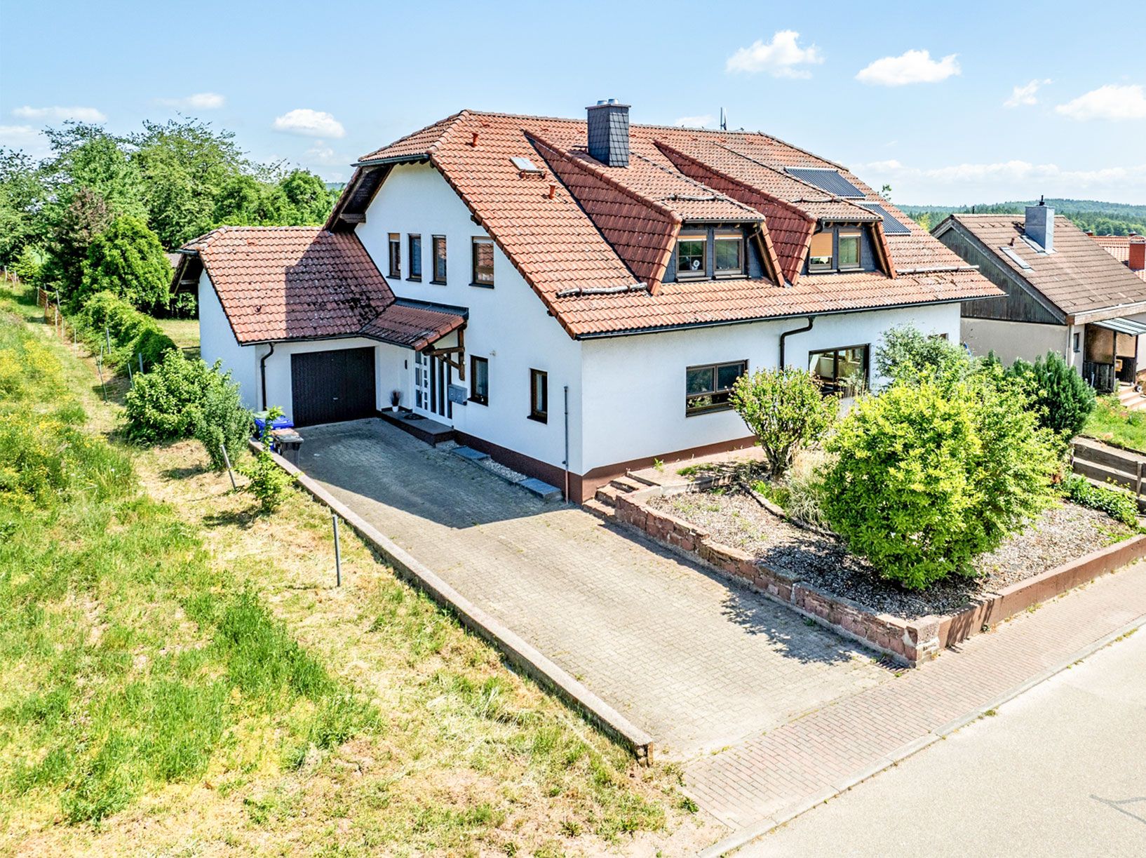 Großes weißes Einfamilienhaus mit rotem Dach, Vorgarten und Einfahrt.