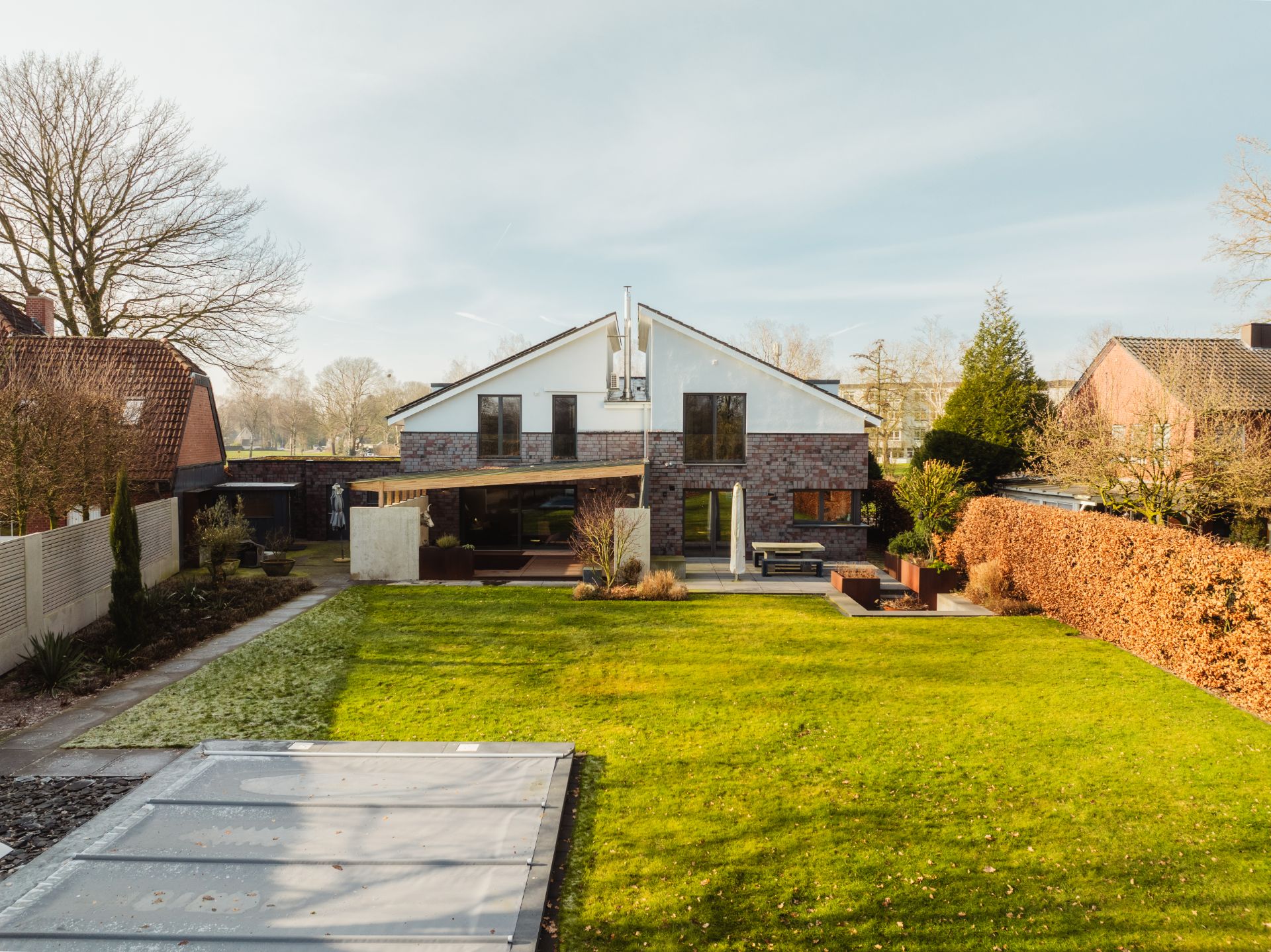 Modernes Wohnhaus mit großem Garten, Rasenfläche und überdachter Terrasse im Hinterhof.