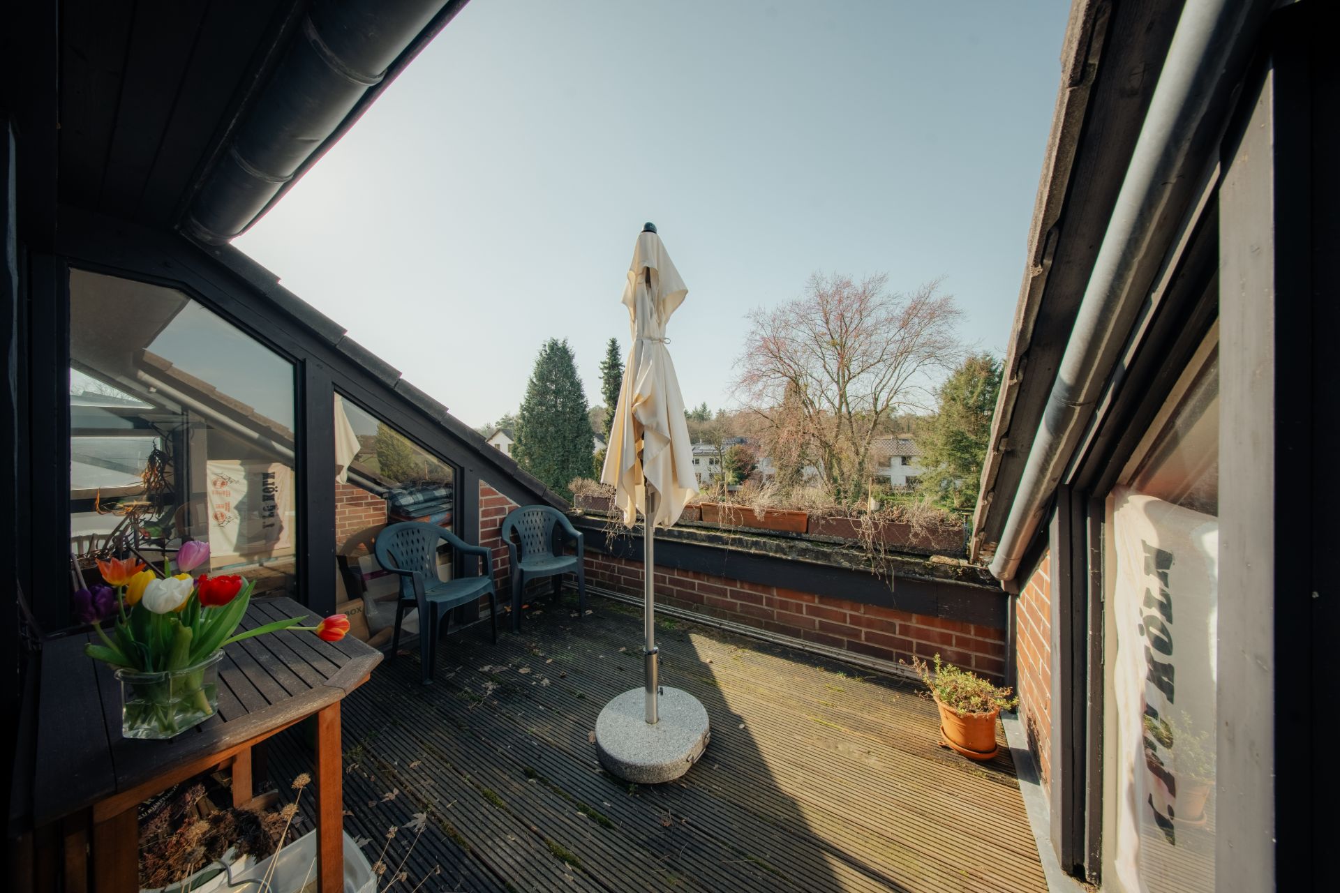 Kleine Dachterrasse mit zwei Stühlen, Tisch mit Blumen, Sonnenschirm und Blumentopf.