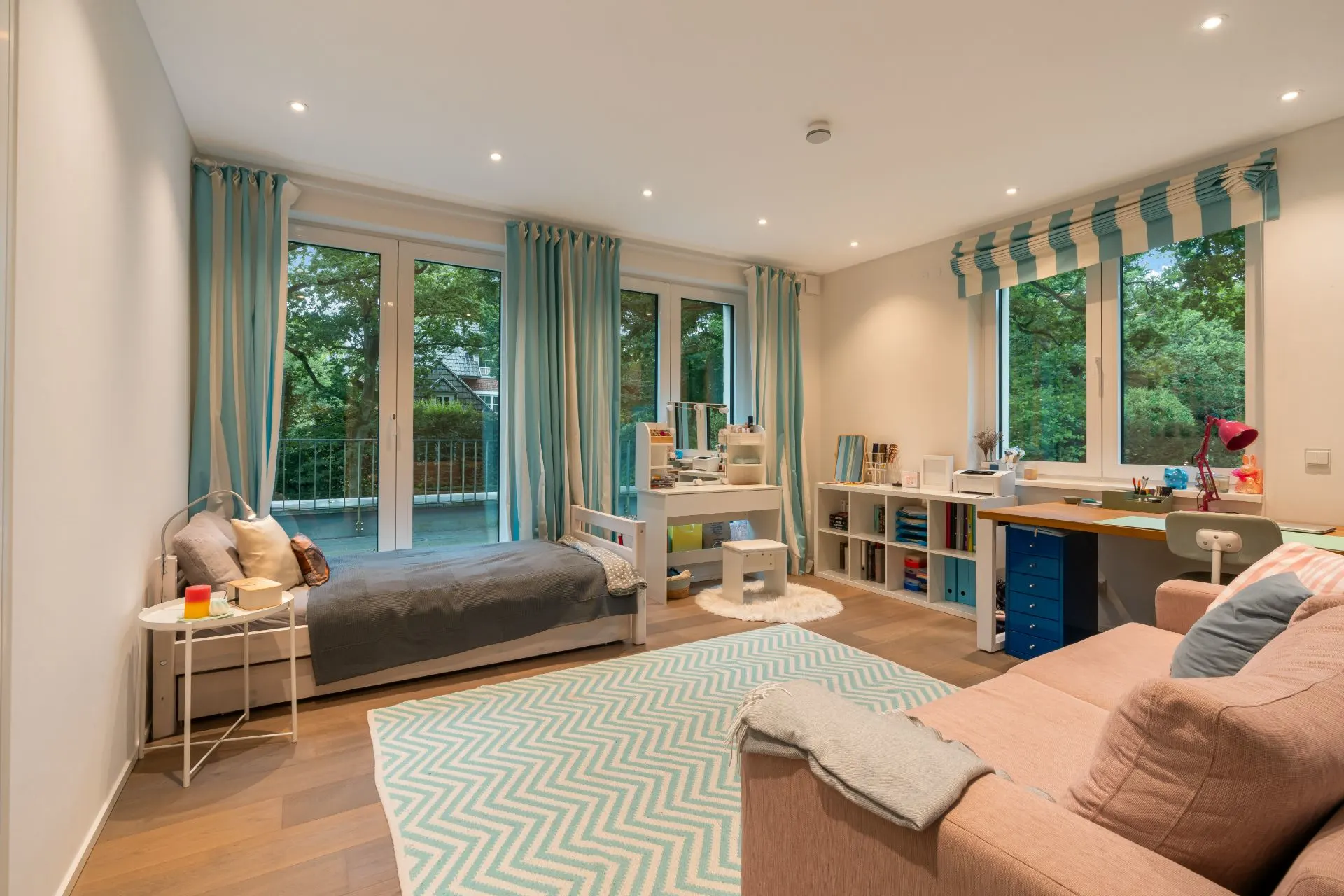 Kinderzimmer mit Bett, Sofa, Schreibtisch und großen Fenstern mit Blick ins Grüne.