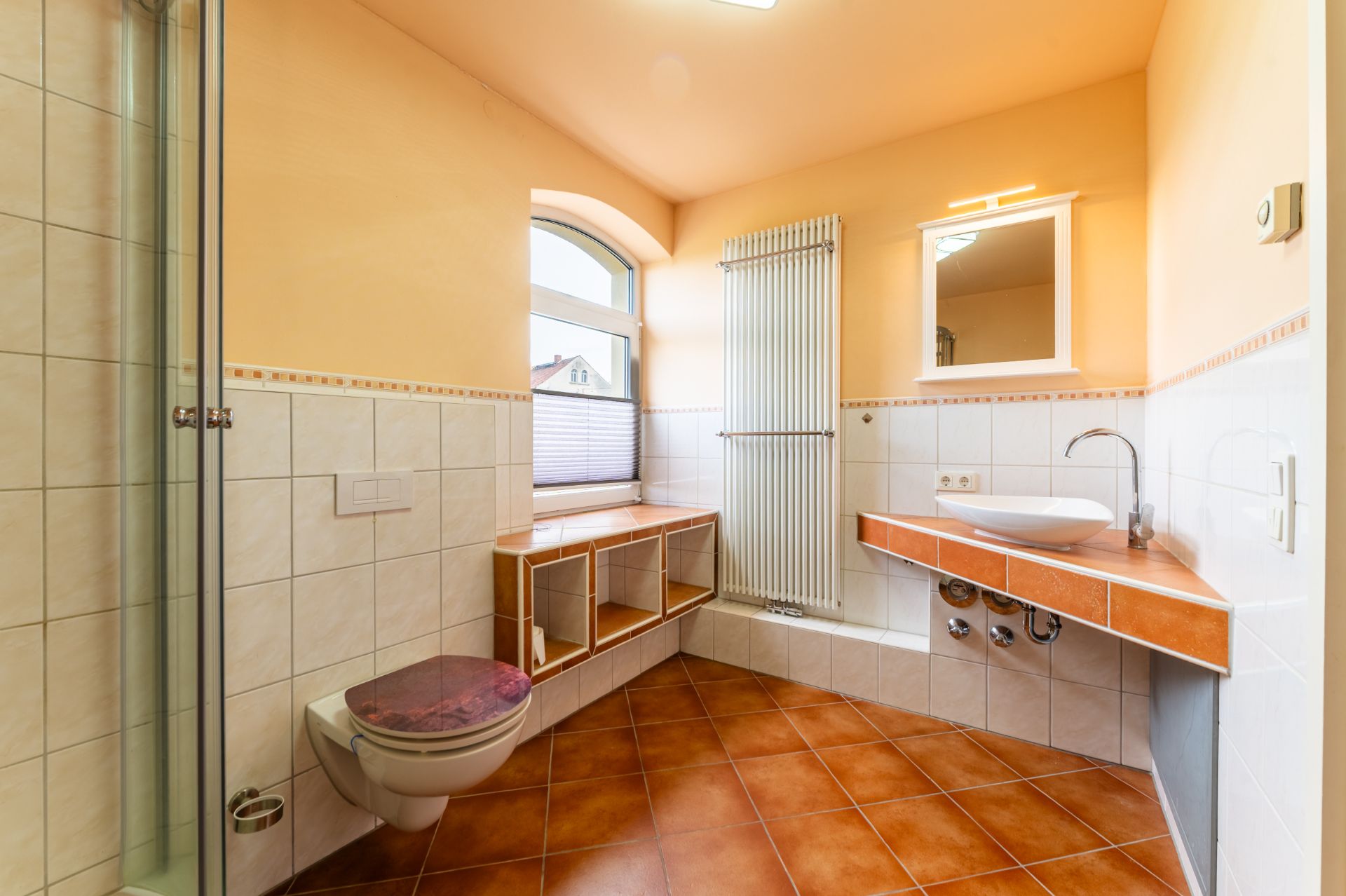 Helles Badezimmer mit Dusche, Wandtoilette, großem Fenster, offenem Regal und Waschbecken mit Spiegel.