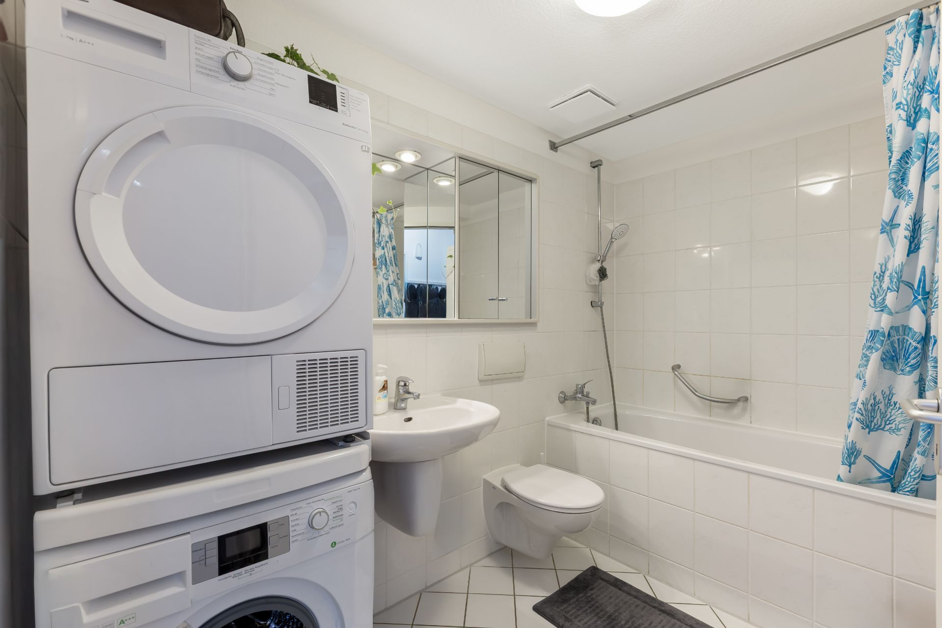 Helles Badezimmer mit Waschmaschine, Trockner, Waschbecken, Toilette und Badewanne mit Duschvorhang.
