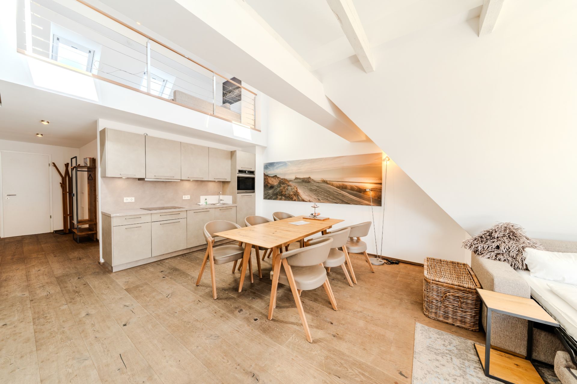 Helles Wohnzimmer mit offener Küche, Esstisch, Stühlen und Sofa unter einer Treppe.