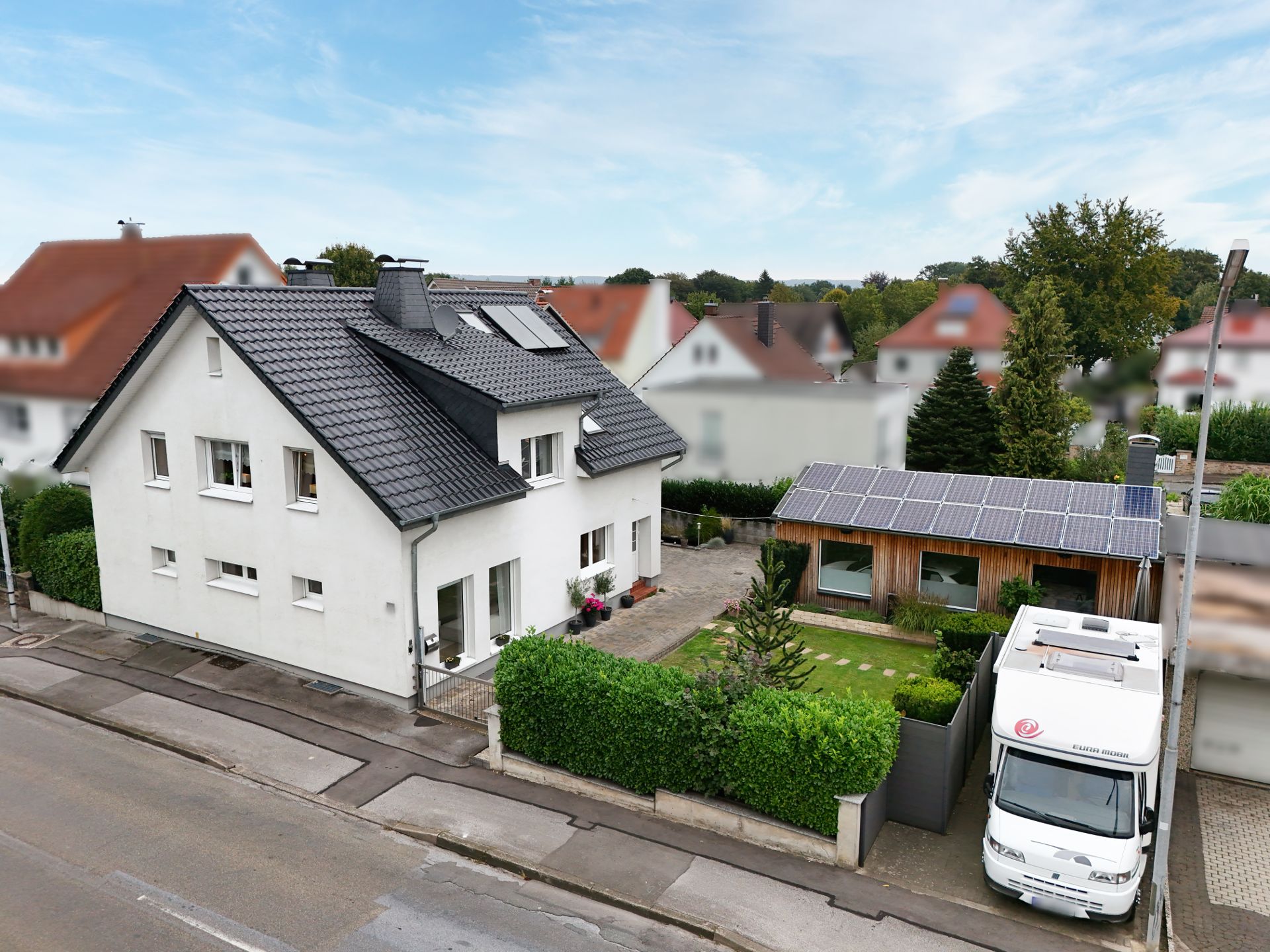 Zweistöckiges Wohnhaus mit Garten, Nebengebäude und Wohnmobil in Einfahrt.