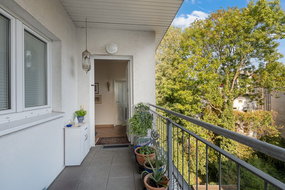 Balkon mit Pflanzentöpfen, Blick ins Grüne, offene Tür zu einer Wohnung.