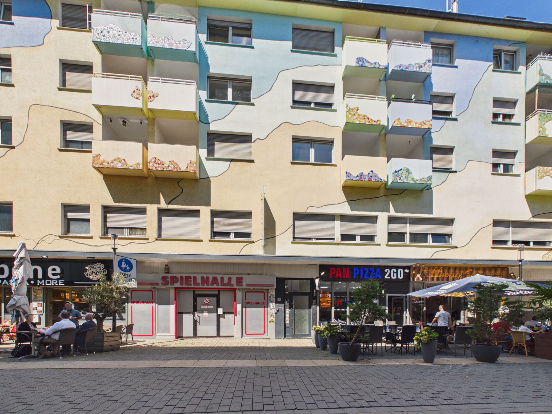 Mehrstöckiges Wohnhaus mit bunten Balkonen und Geschäften im Erdgeschoss.