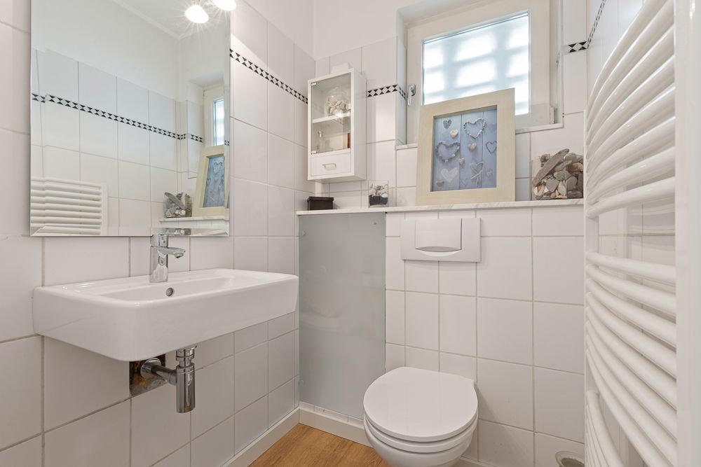 Kleines, modernes Badezimmer mit weißem Waschbecken, Wandtoilette und Spiegel.