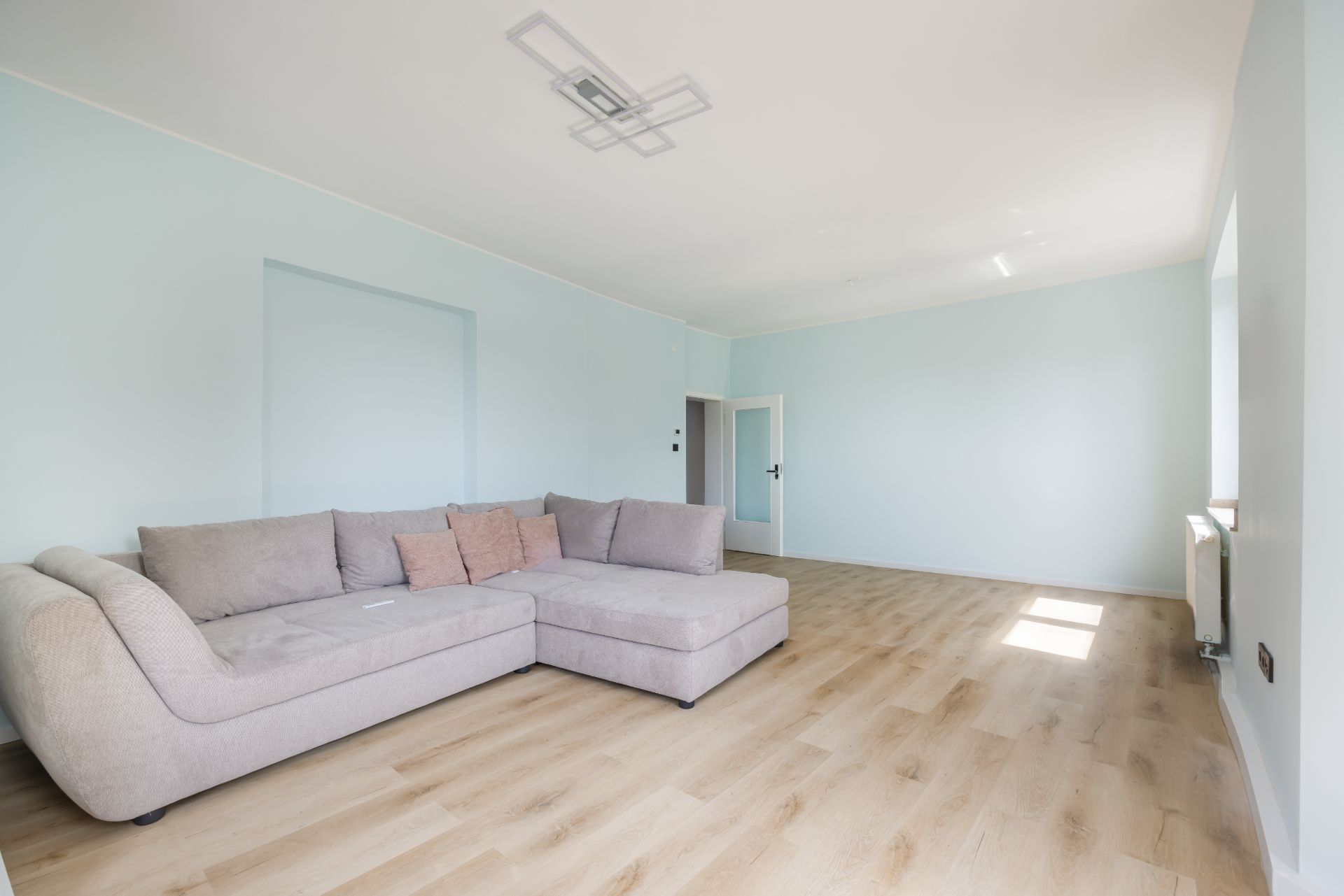 Helles Wohnzimmer mit großem, grauen Ecksofa und Holzfußboden.