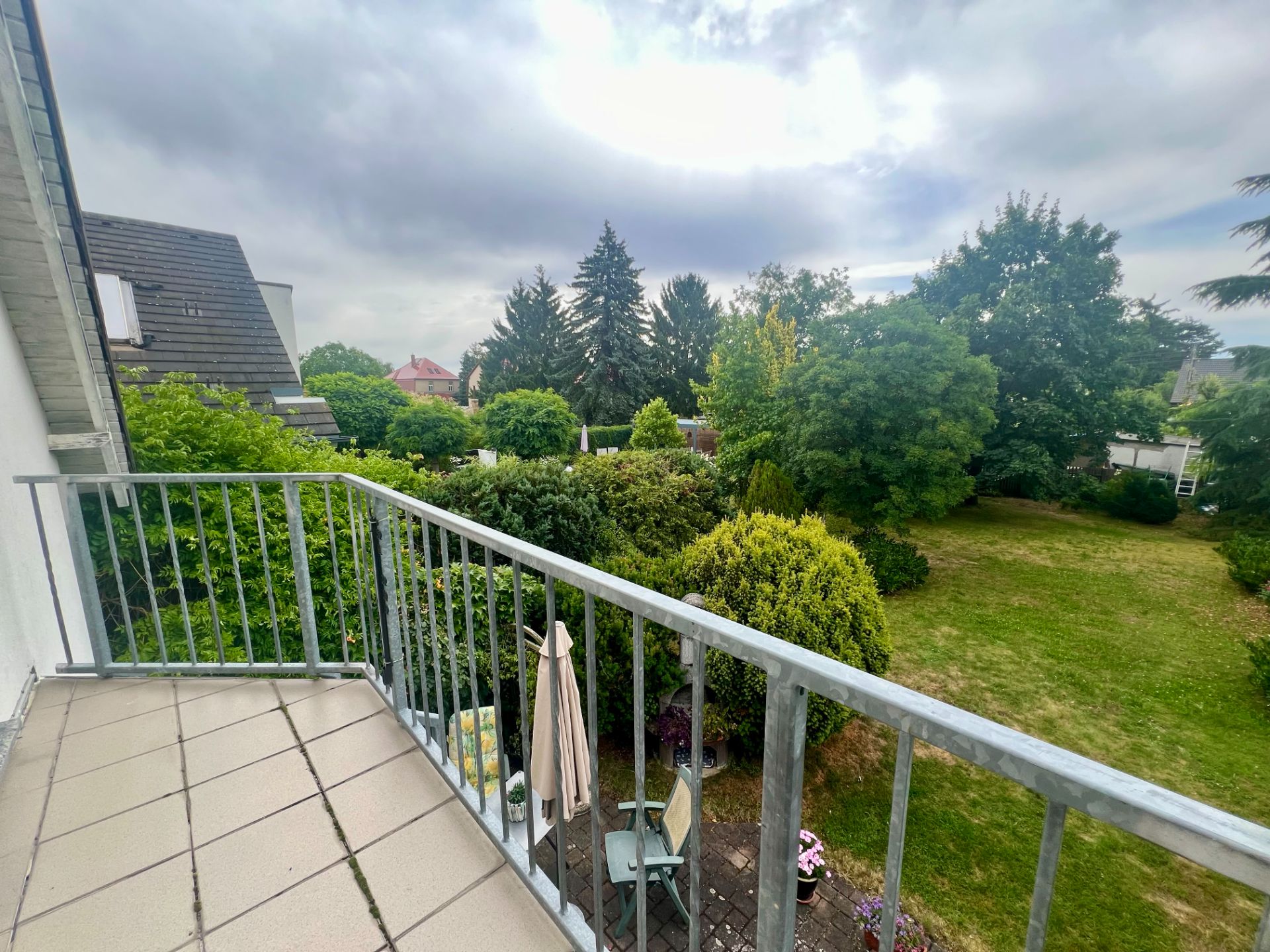 Balkon mit Fliesenboden und Blick auf einen großen grünen Garten mit Bäumen.