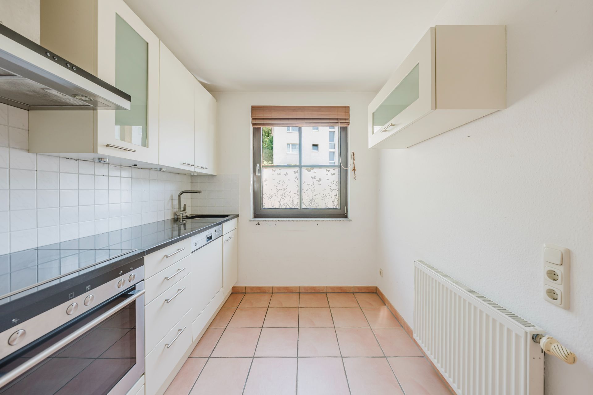 Helle Küche mit weißen Schränken, Fenster, Herd, Spüle und Fliesenboden.