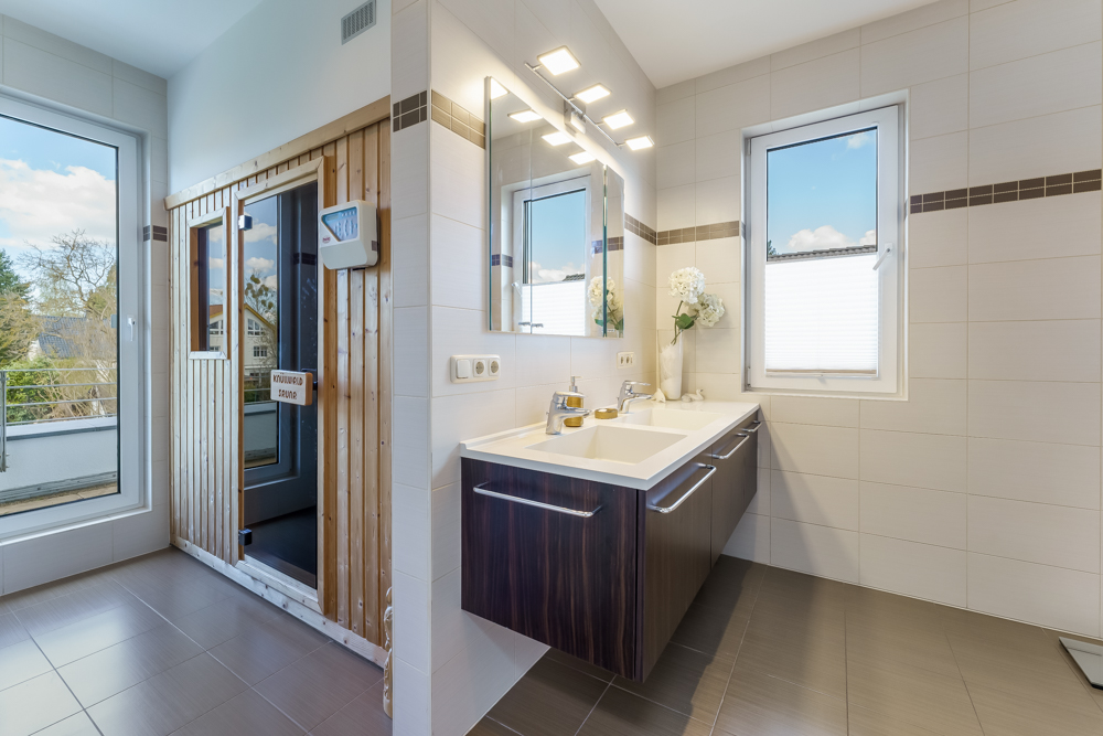 Modernes Badezimmer mit Doppelwaschbecken, großem Fenster und einer Holzsauna.