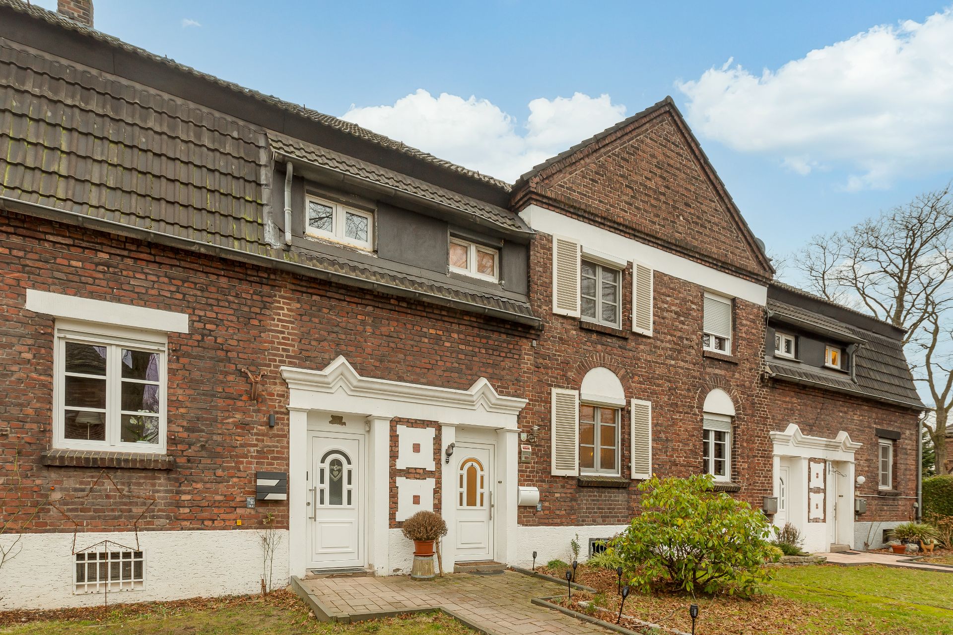 Mehrfamilienhaus aus roten Backsteinen mit weißen Fenstern und Türen, kleiner Vorgarten.