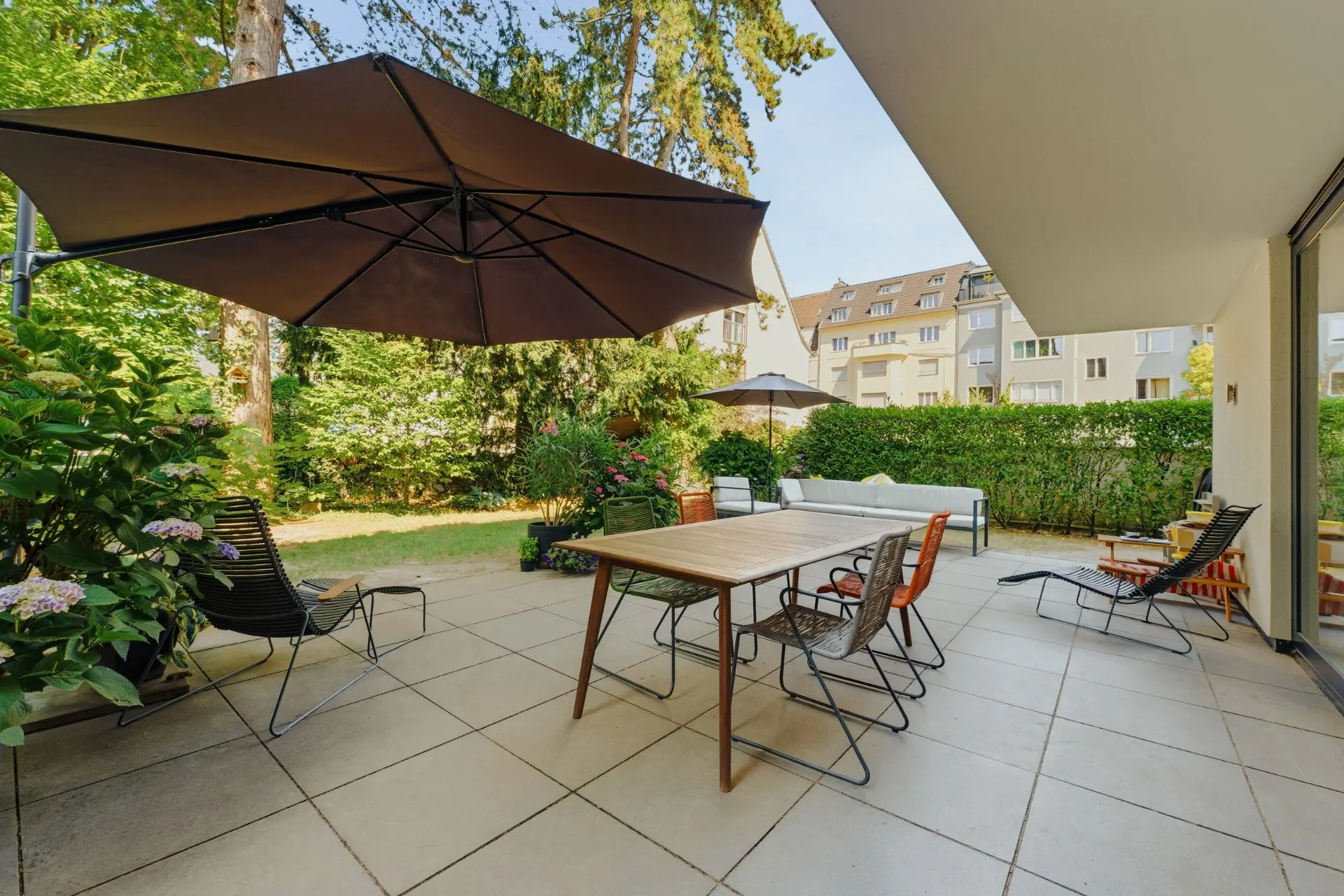 Große Terrasse mit Esstisch, Stühlen, Liegestühlen und Sonnenschirm im Garten.