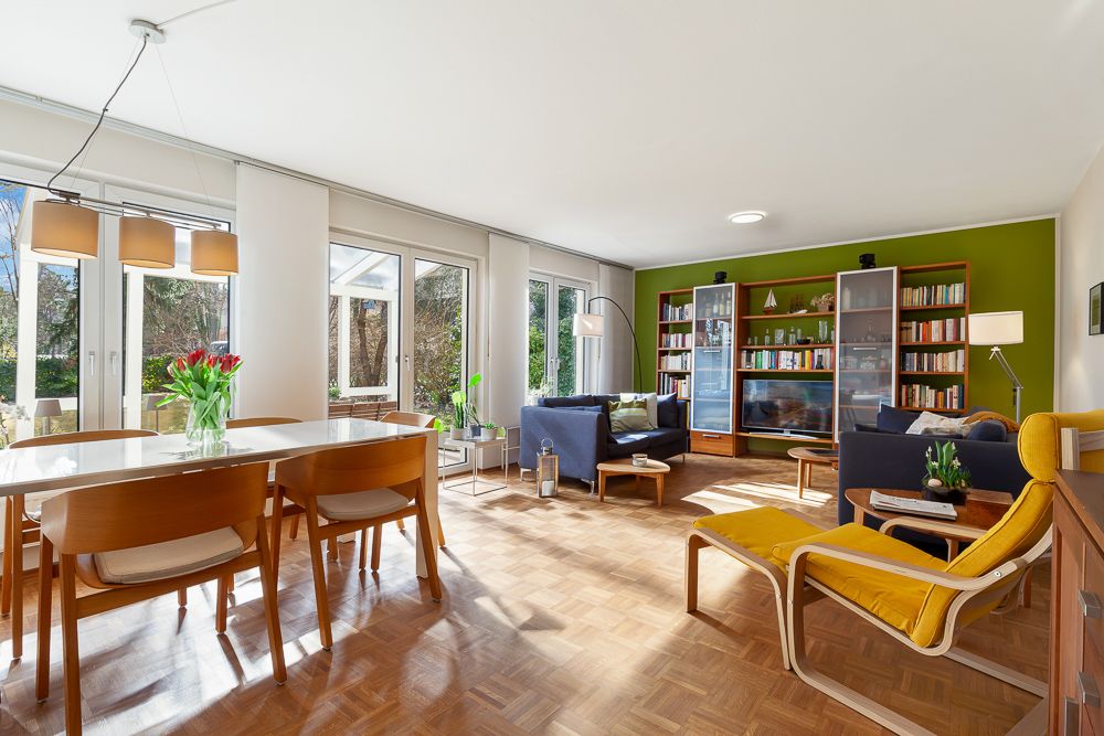 Helles Wohnzimmer mit Essbereich, großen Fenstern, Bücherregal und gelbem Sessel.