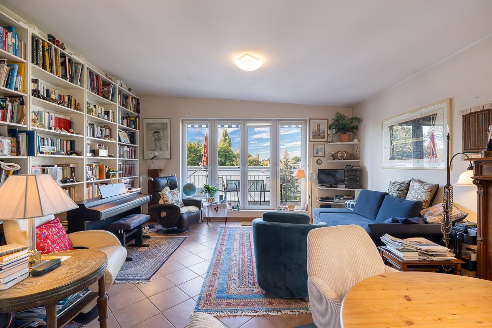 Helles Wohnzimmer mit Bücherregal, Sofa, Klavier und großem Fenster mit Blick nach draußen.
