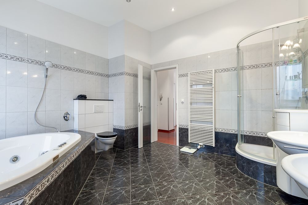 Modernes Badezimmer mit Badewanne, Dusche, Toilette, Waschbecken und Handtuchheizkörper.